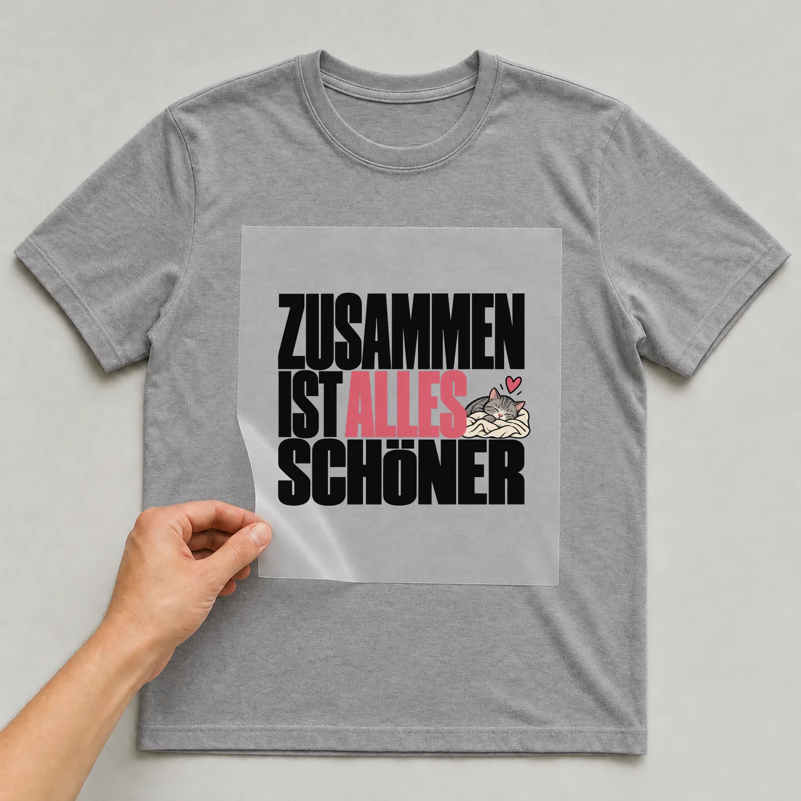 Bügelbild „Zusammen ist alles schöner“ (kompakter Plakatschrift) auf grauem T-Shirt, Folie wird aufgelegt