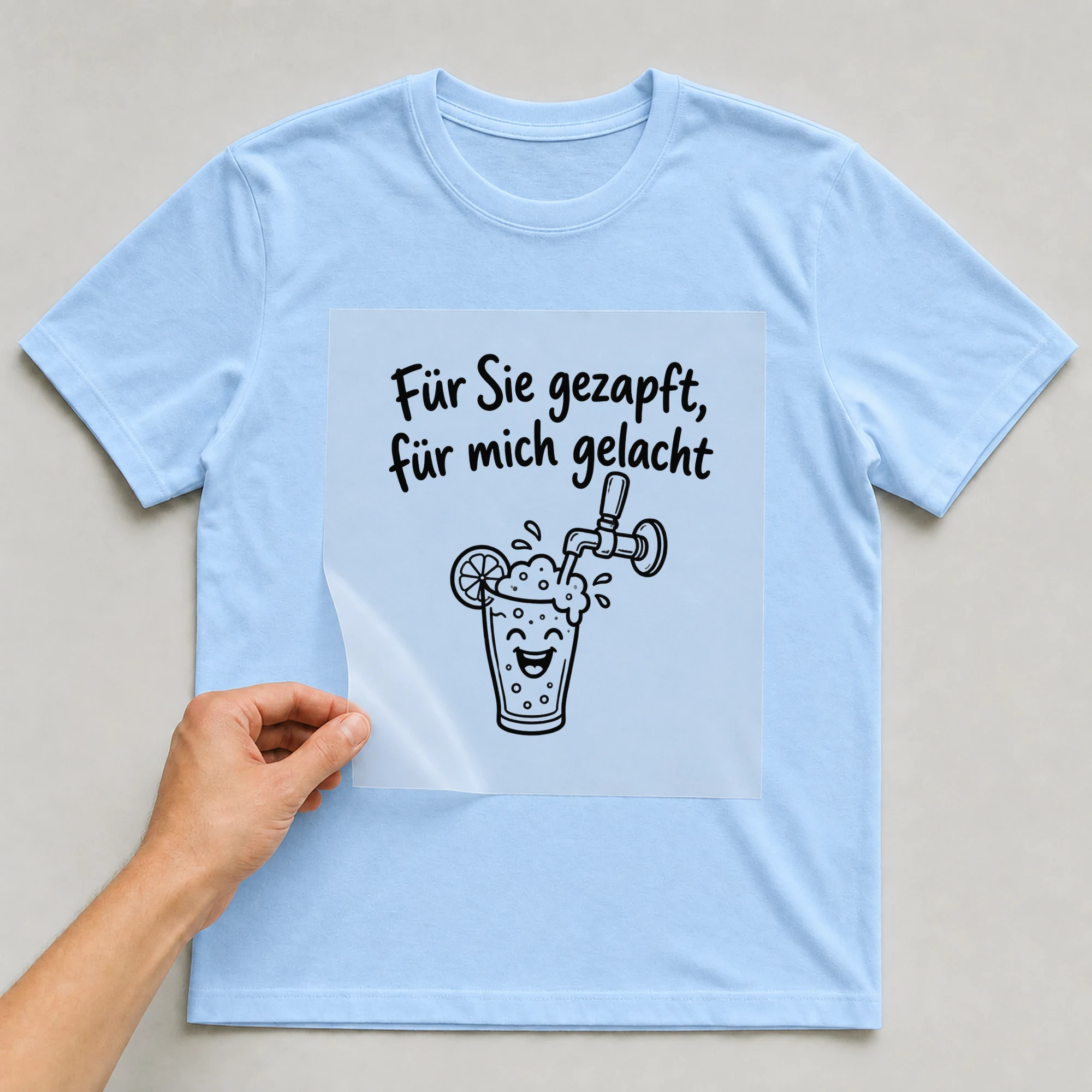 Bügelbild „Für Sie gezapft, für mich gelacht“ auf babyblauem T-Shirt, Folie wird aufgelegt