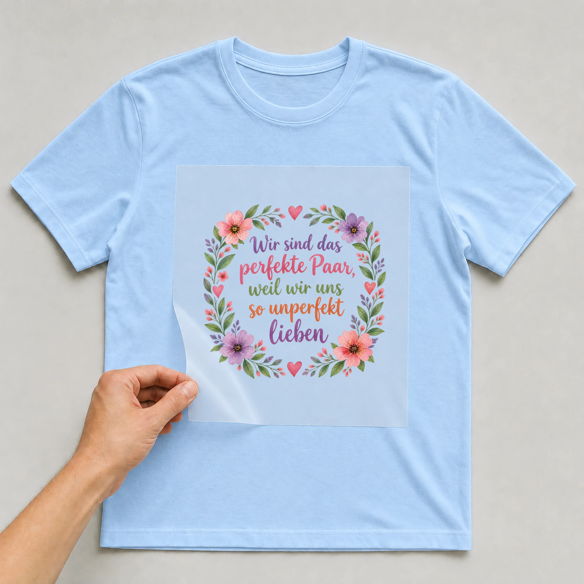 Bügelbild „Wir sind das perfekte Paar, weil wir uns so unperfekt lieben“ auf babyblauem T-Shirt, Folie wird aufgelegt