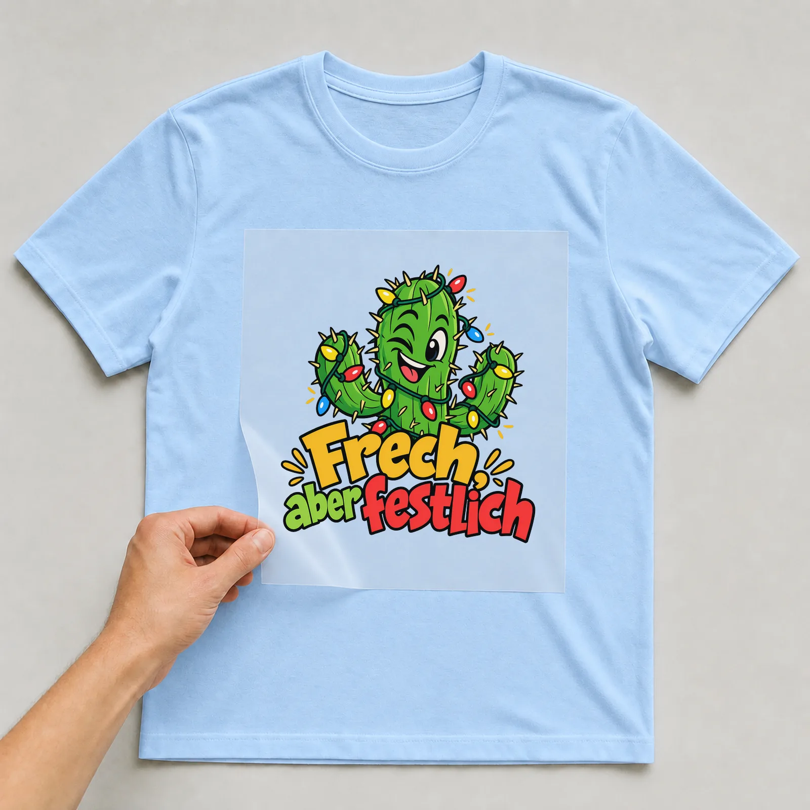 Bügelbild „Frech, aber festlich“ auf hellblauem T-Shirt, Folie wird aufgelegt