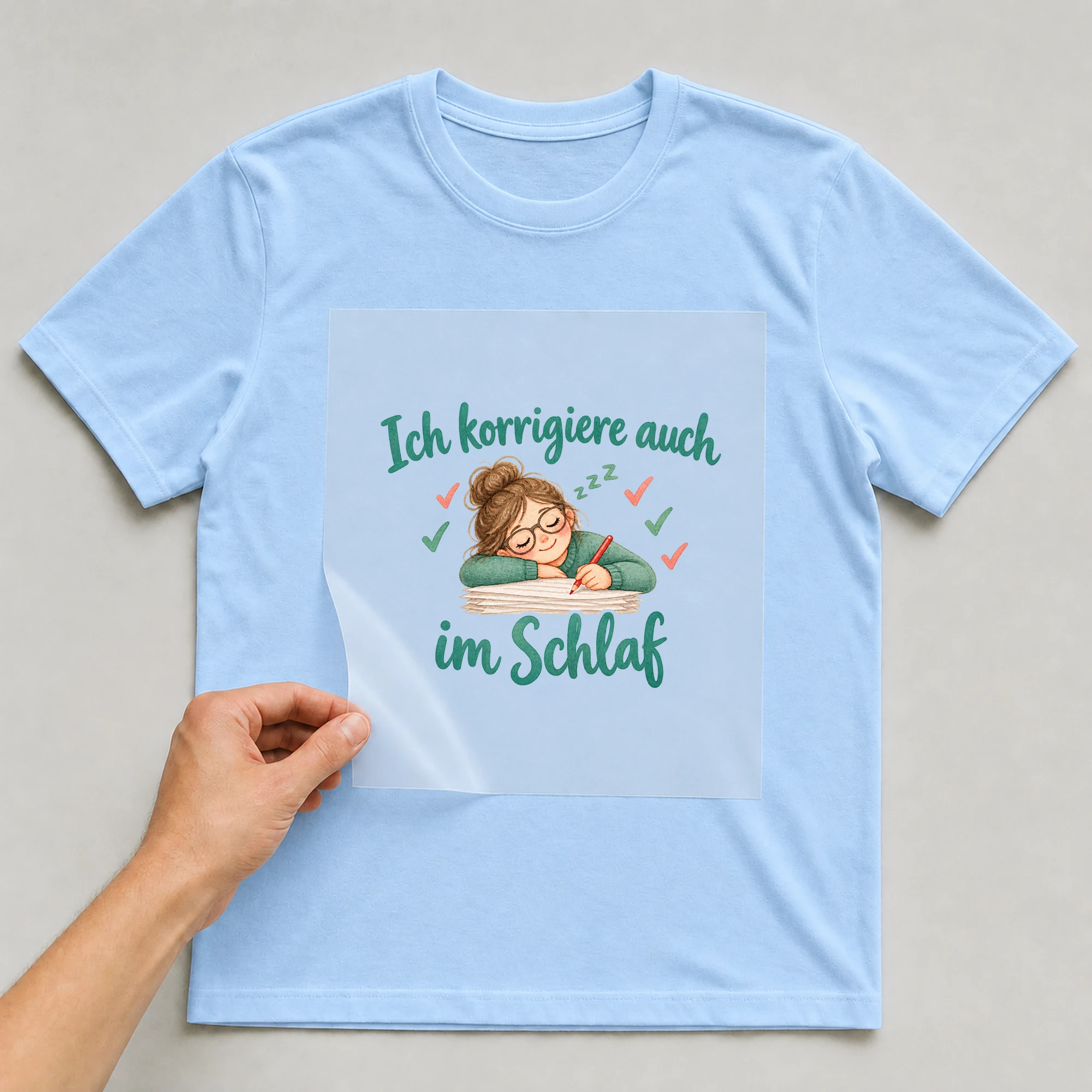 Bügelbild „Ich korrigiere auch im Schlaf“ auf babyblauem T-Shirt, Folie wird aufgelegt