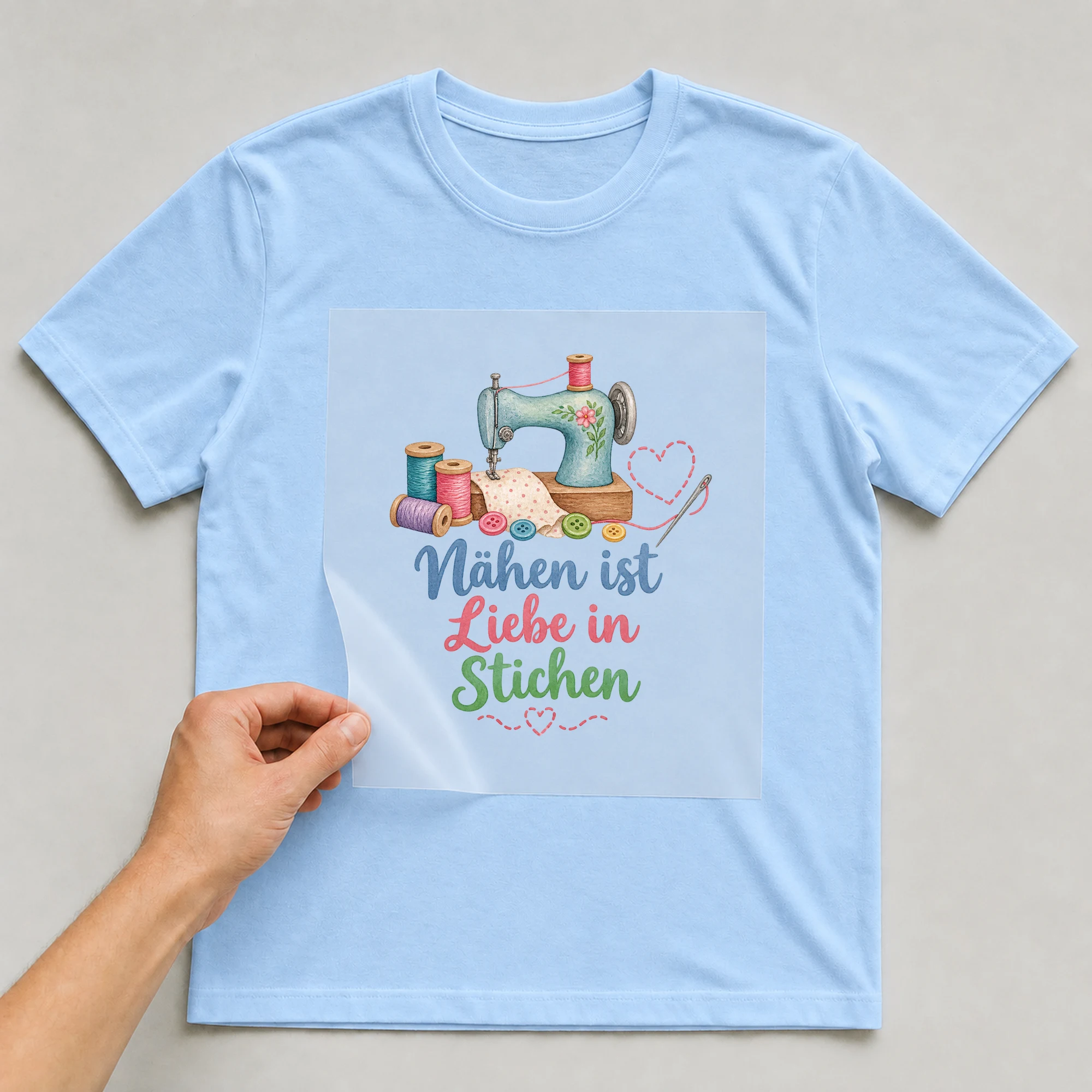 Bügelbild „Nähen ist Liebe in Stichen“ auf babyblauem T-Shirt, Folie wird aufgelegt