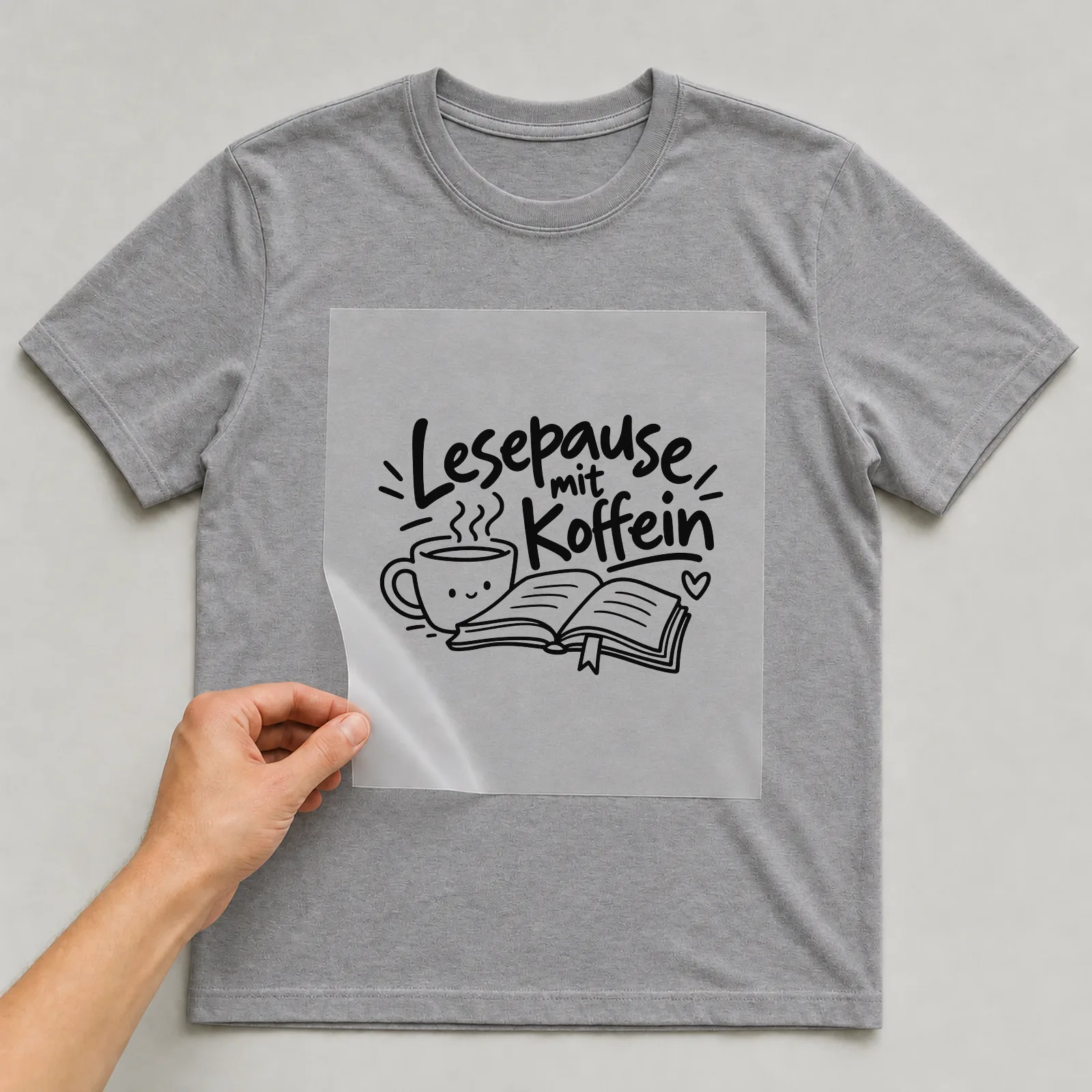 Bügelbild „Lesepause mit Koffein“ auf grauem T-Shirt, Folie wird aufgelegt