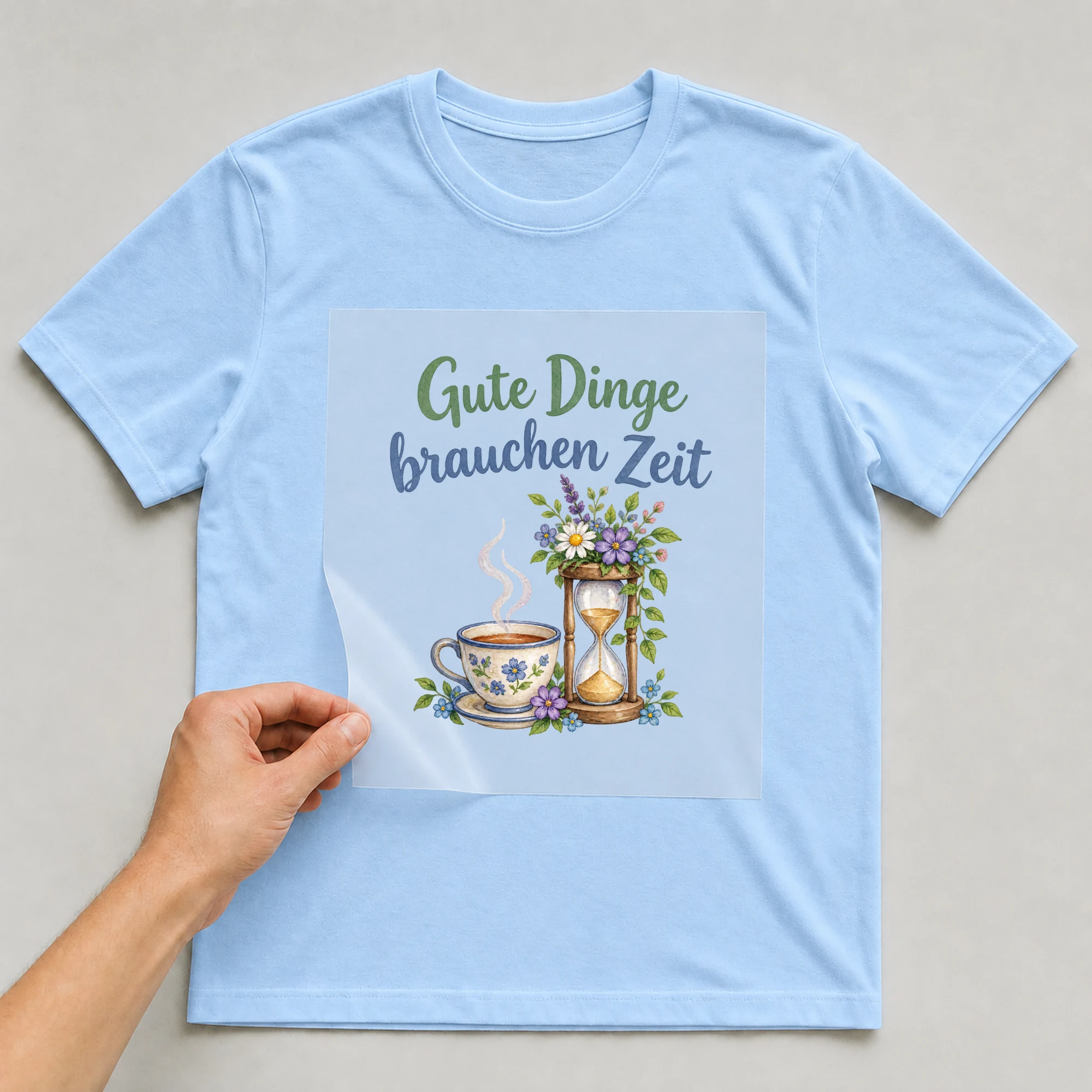 Bügelbild „Gute Dinge brauchen Zeit“ auf babyblauem T-Shirt, Folie wird aufgelegt