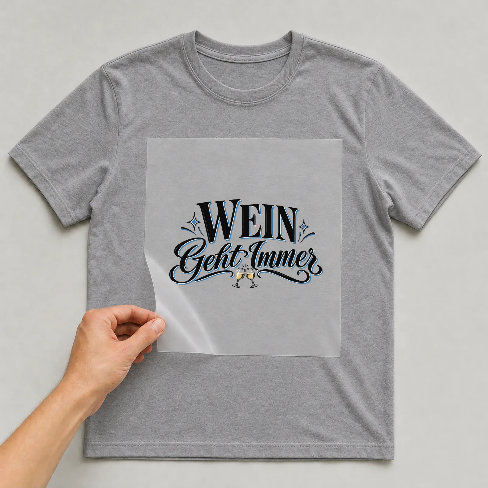 Bügelbild „Wein geht immer“ (klassischem Schriftmix) auf grauem T-Shirt, Folie wird aufgelegt