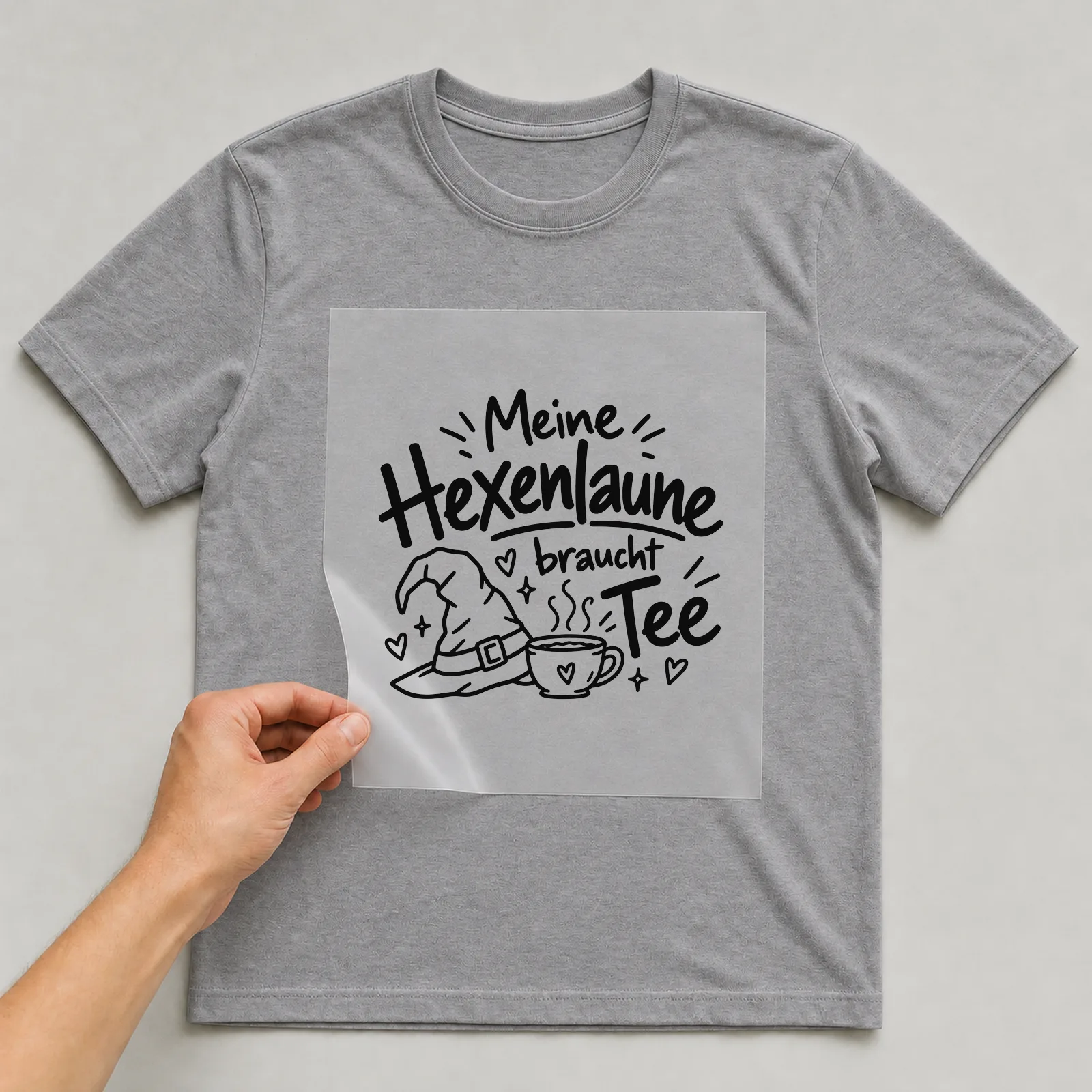 Bügelbild „Meine Hexenlaune braucht Tee“ auf grauem T-Shirt, Folie wird aufgelegt