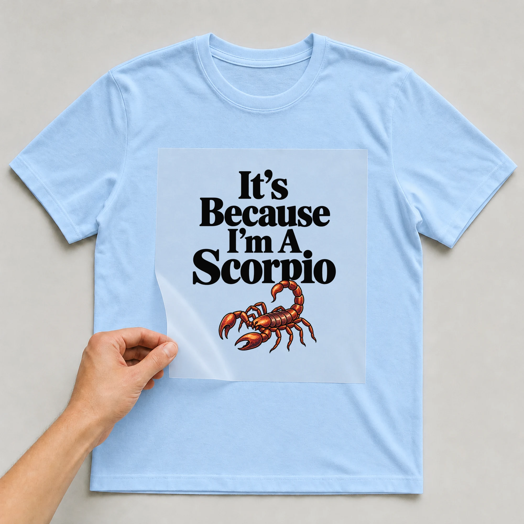 Bügelbild „It's Because I'm A Scorpio“ auf babyblauem T-Shirt, Folie wird aufgelegt