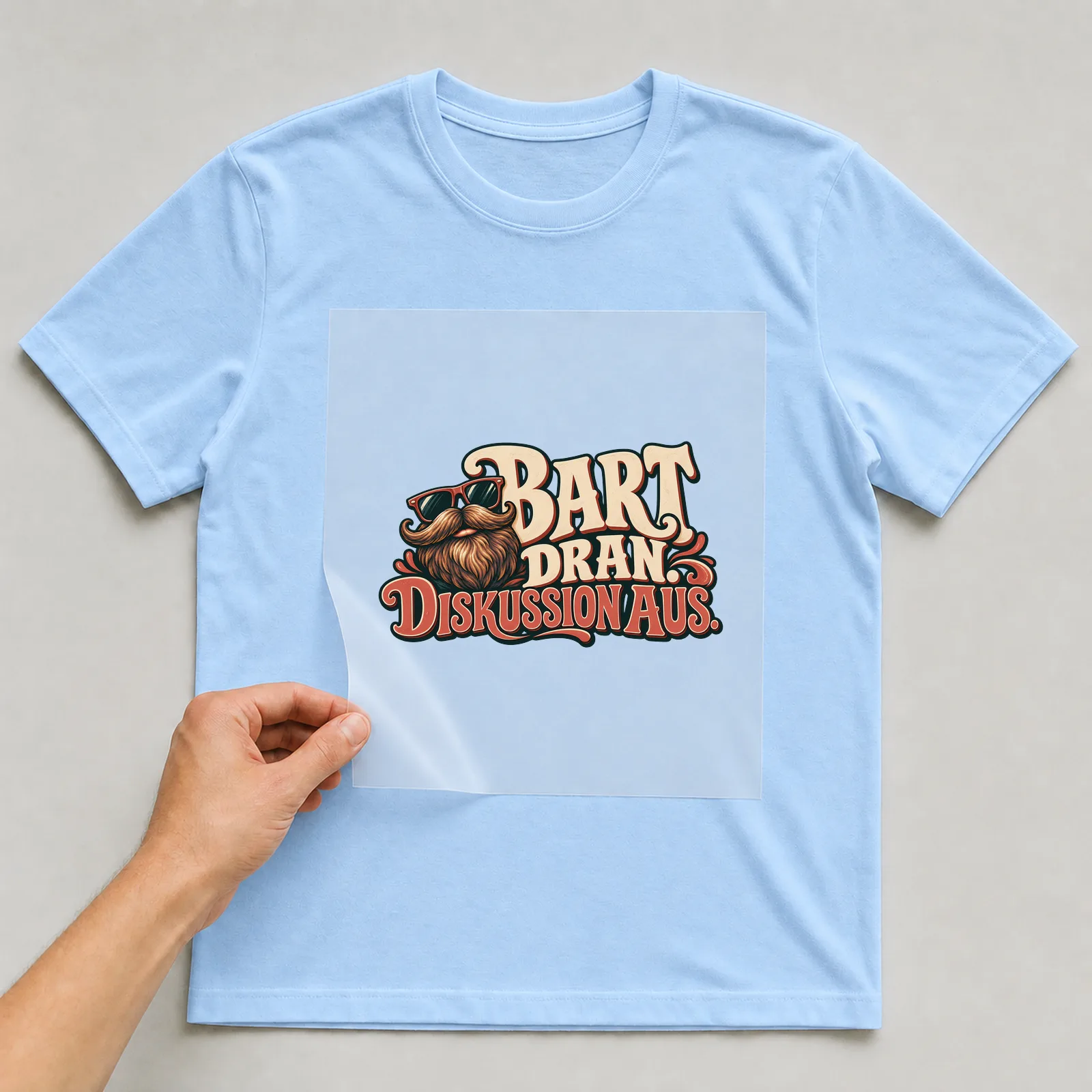Bügelbild „Bart dran. Diskussion aus.“ auf hellblauem T-Shirt, Folie wird aufgelegt