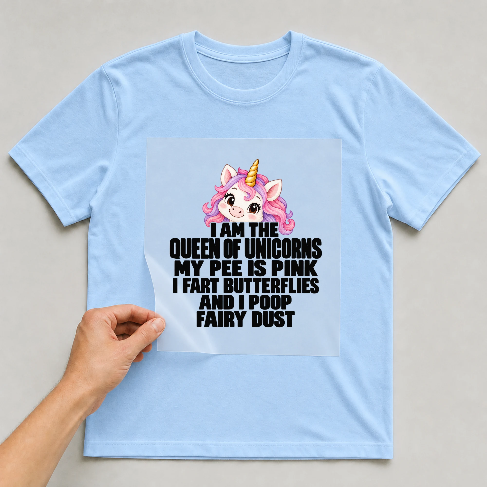 Bügelbild „I Am The Queen Of Unicorns My Pee Is Pink I Fart Butterflies And I Poop Fairy“ auf babyblauem T-Shirt, Folie wird aufgelegt