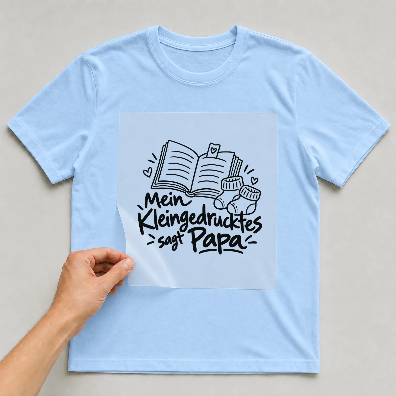 Bügelbild „Mein Kleingedrucktes sagt Papa“ auf hellblauem T-Shirt, Folie wird aufgelegt