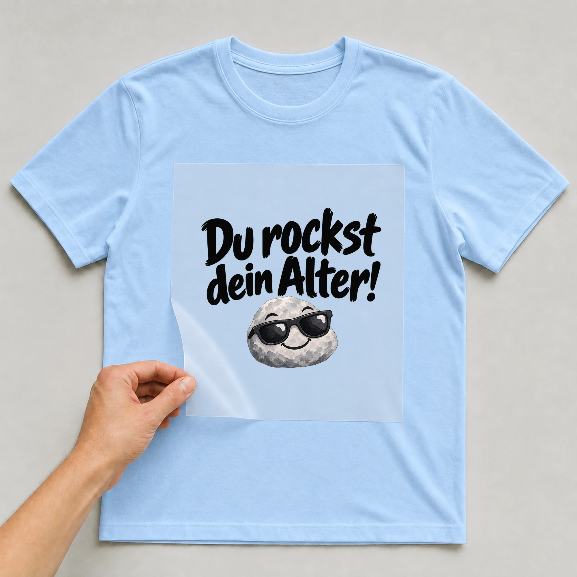 Bügelbild „Du rockst dein Alter!“ auf babyblauem T-Shirt, Folie wird aufgelegt