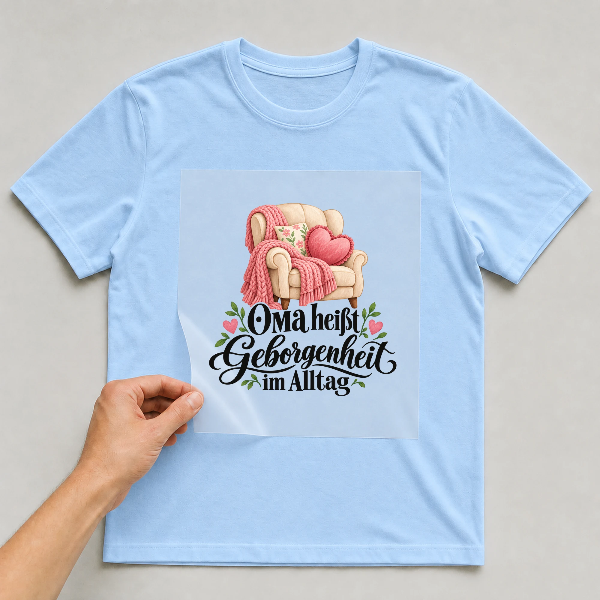 Bügelbild „OMA heißt Geborgenheit im Alltag“ auf hellblauem T-Shirt, Folie wird aufgelegt
