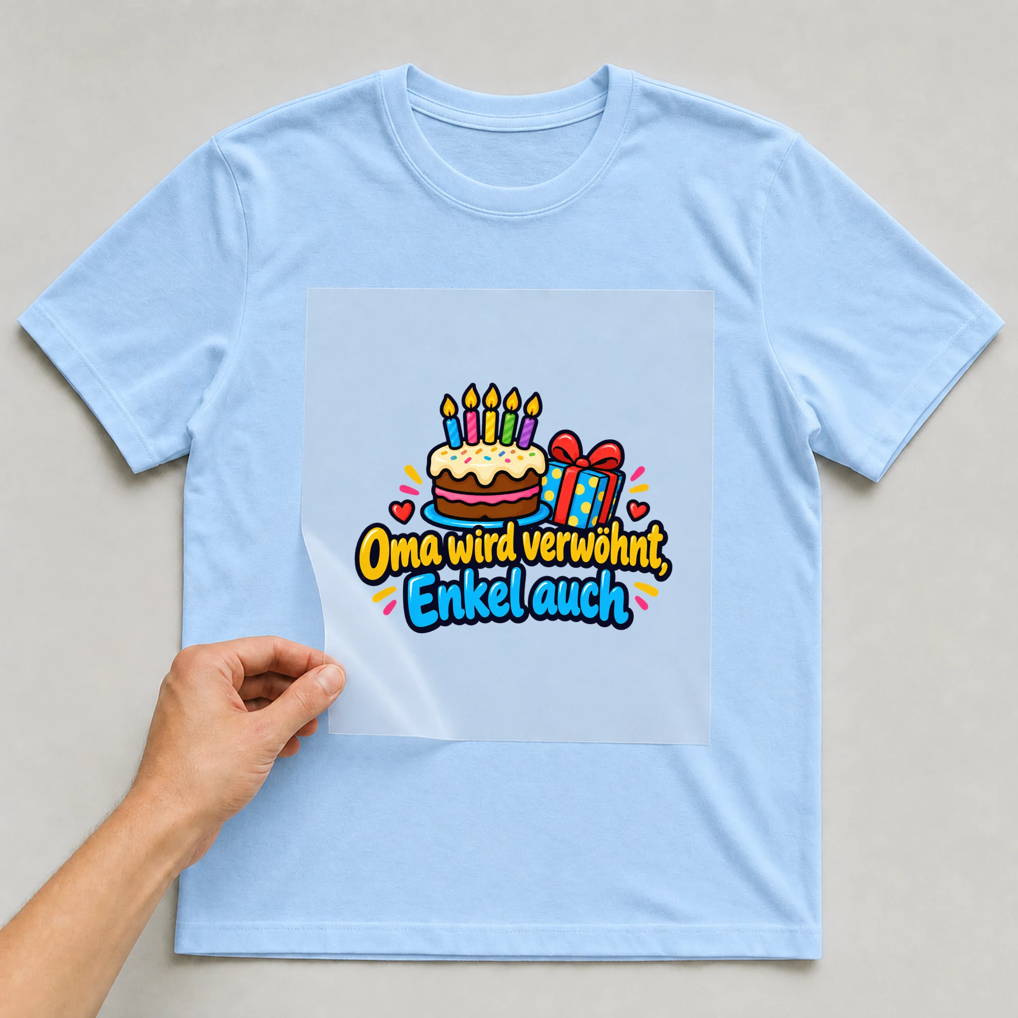 Bügelbild „Oma wird verwöhnt, Enkel auch“ auf babyblauem T-Shirt, Folie wird aufgelegt