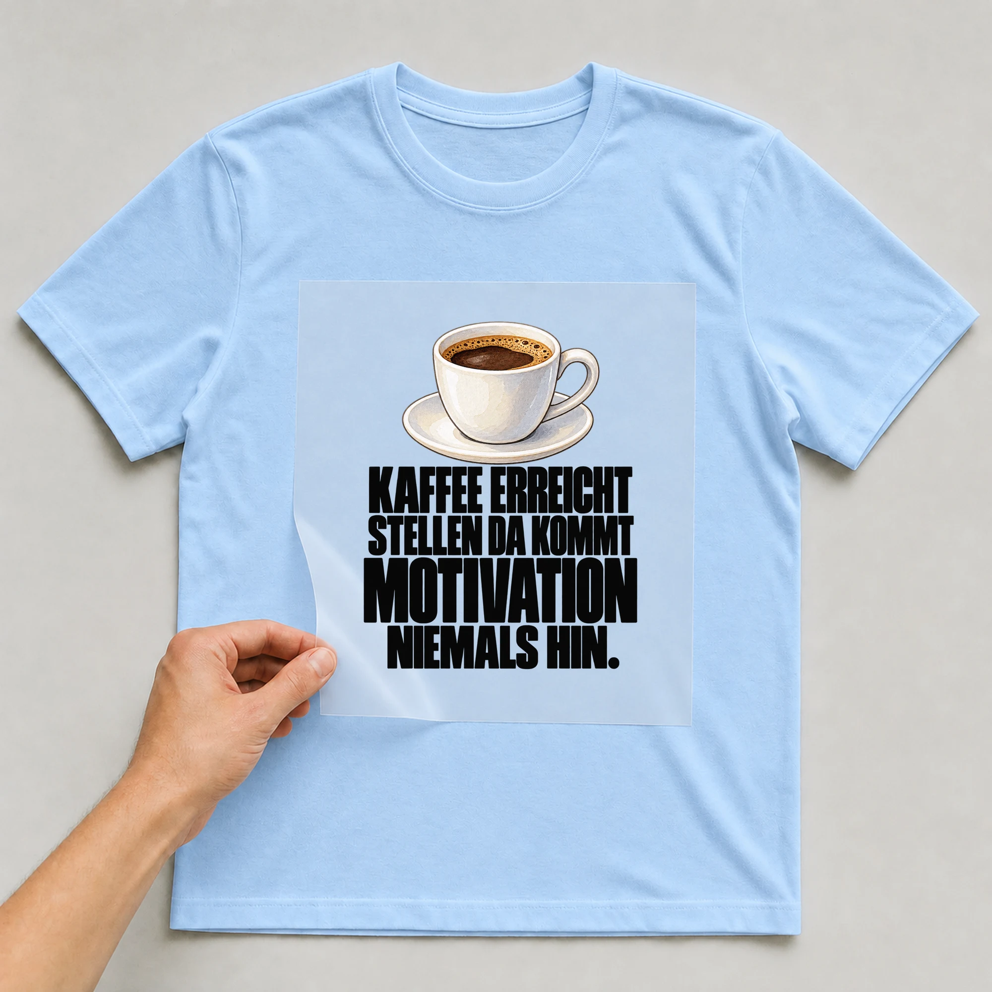 Bügelbild „Kaffee erreicht stellen da kommt Motivation niemals hin.“ auf babyblauem T-Shirt, Folie wird aufgelegt