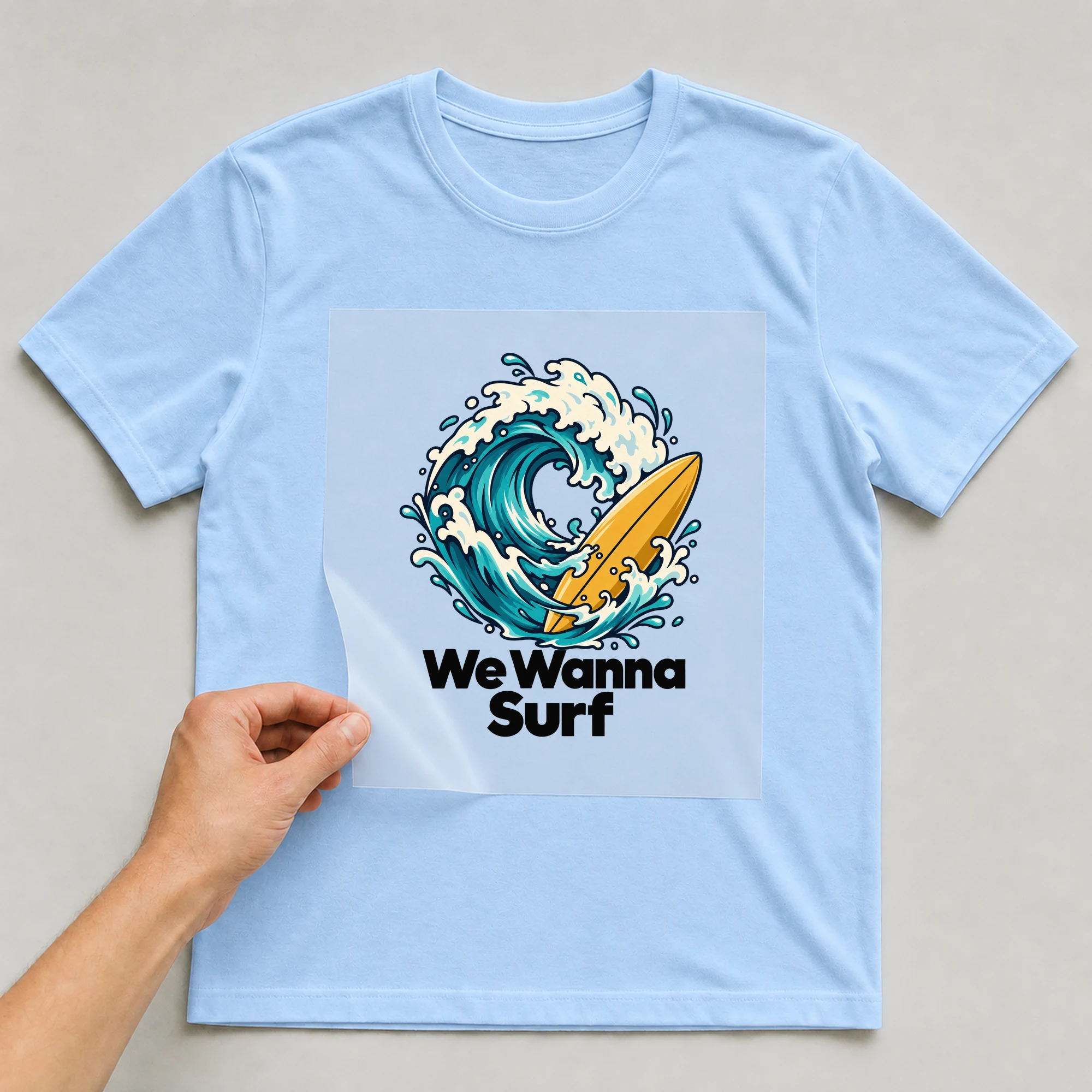 Bügelbild „We Wanna Surf“ auf babyblauem T-Shirt, Folie wird aufgelegt