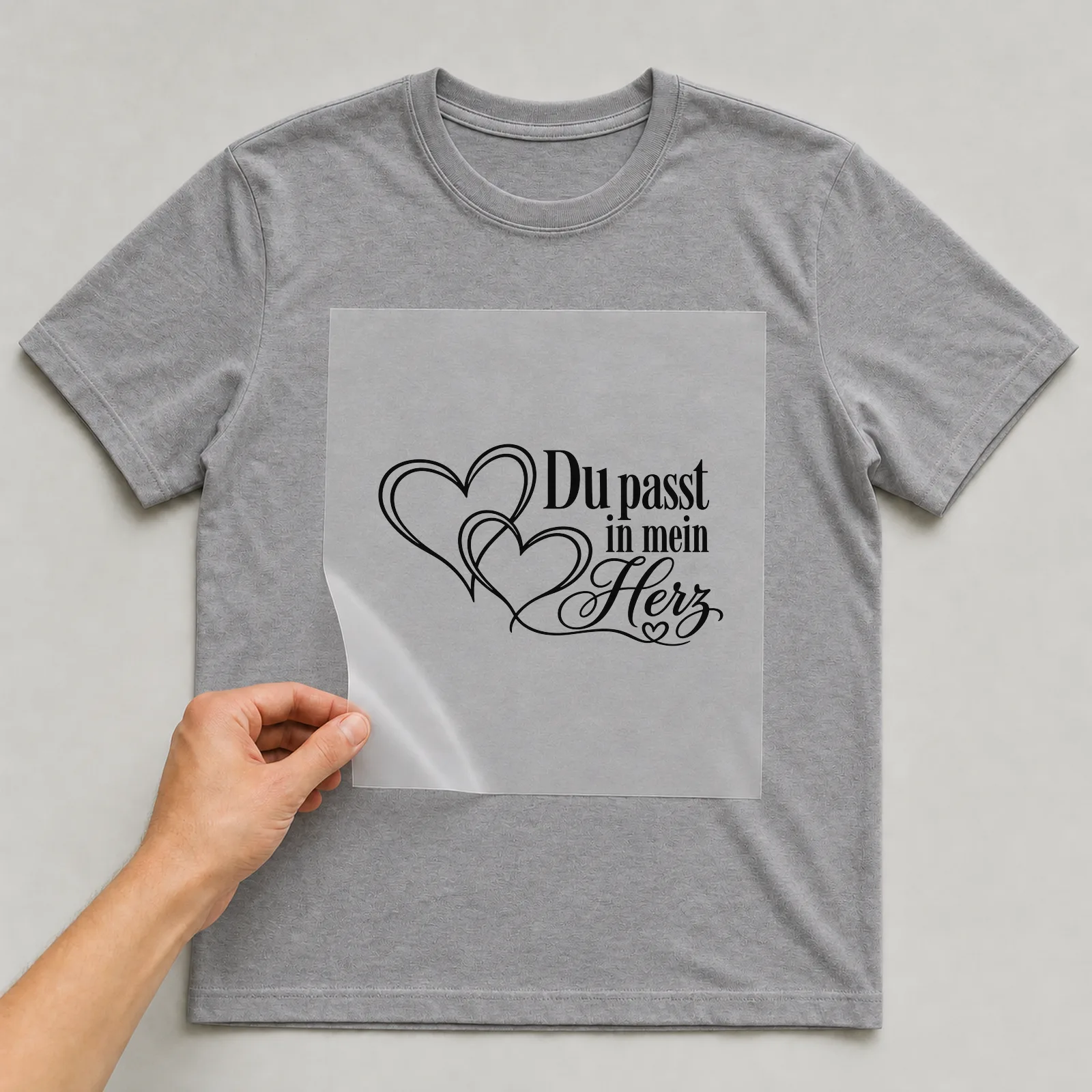 Bügelbild „Du passt in mein Herz“ auf grauem T-Shirt, Folie wird aufgelegt