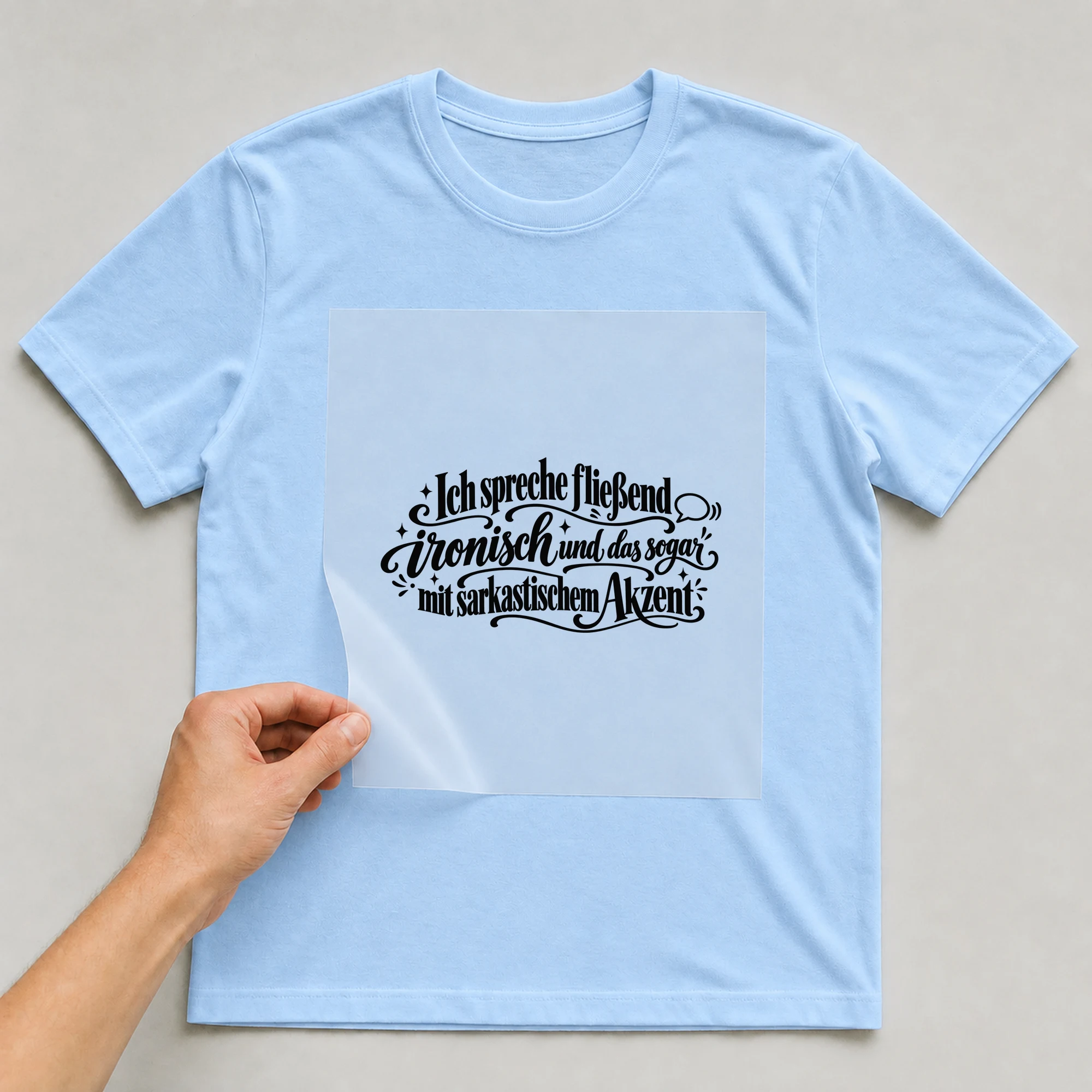 Bügelbild „Ich spreche fließend ironisch, mit sarkastischem Akzent“ auf babyblauem T-Shirt, Folie wird aufgelegt