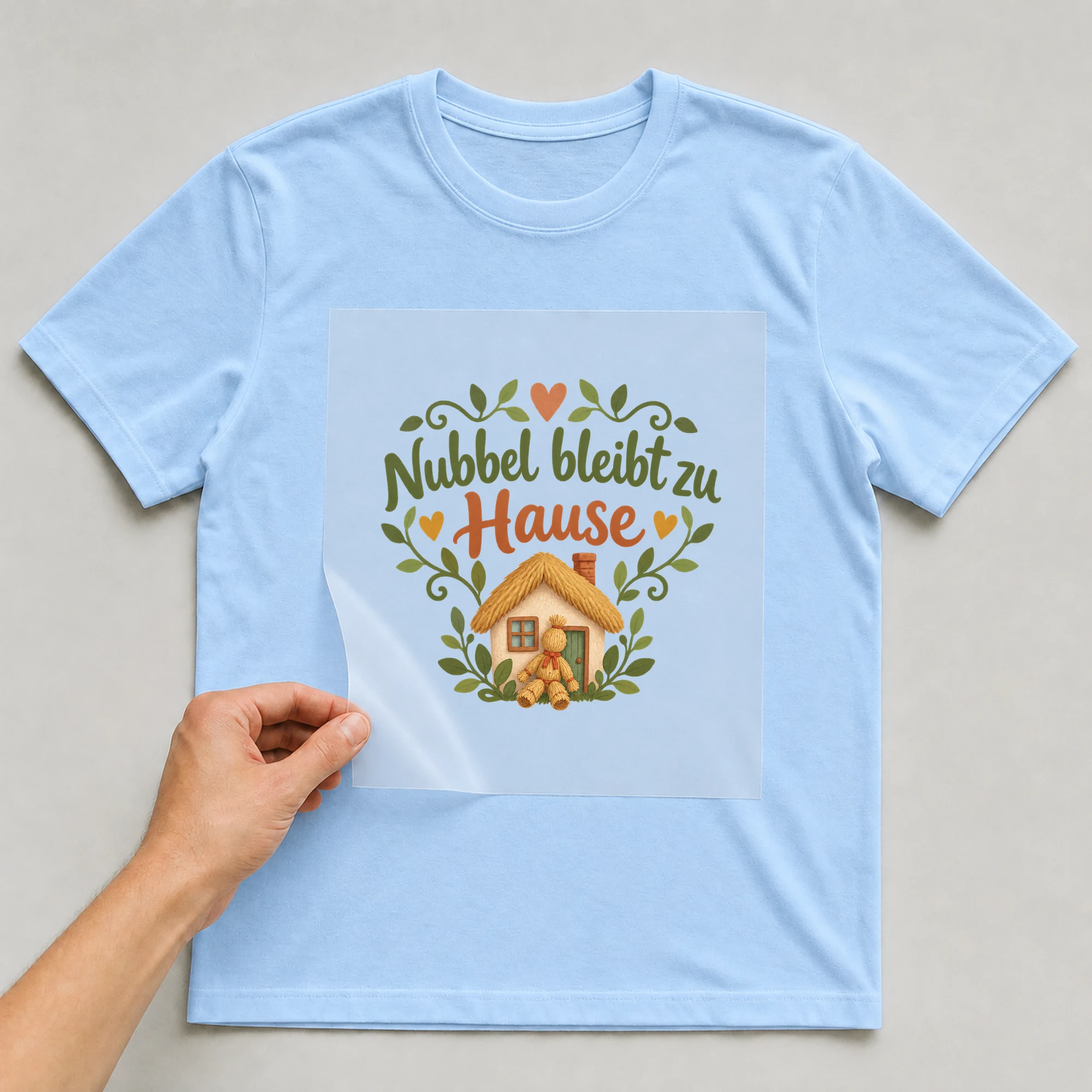 Bügelbild „Nubbel bleibt zu Hause“ auf babyblauem T-Shirt, Folie wird aufgelegt