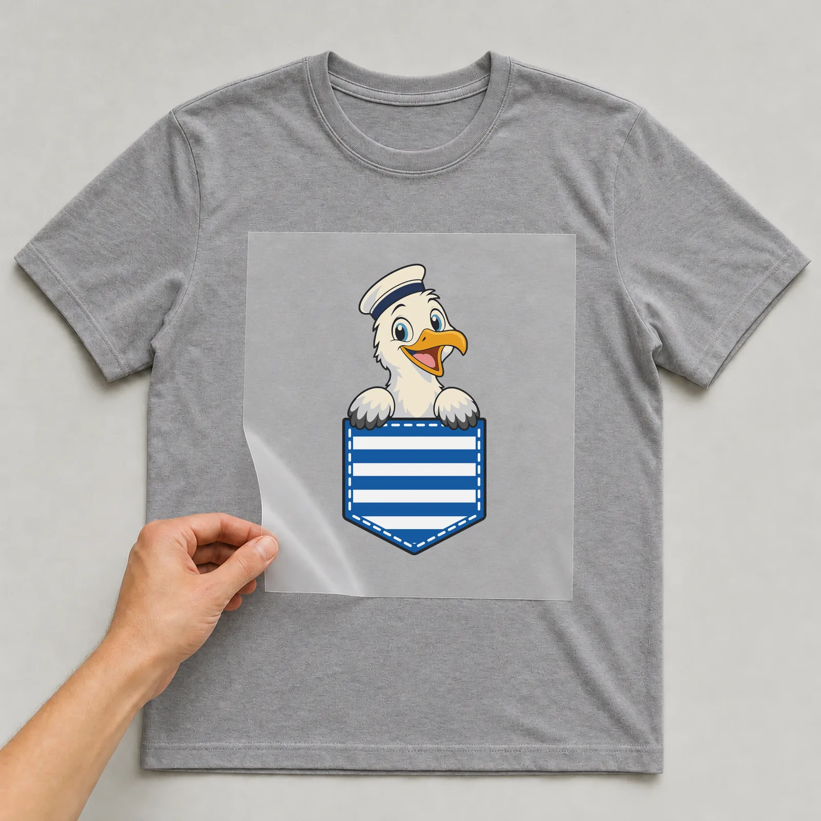 Bügelbild Brusttasche Möwe Matrose auf grauem T-Shirt, Folie wird aufgelegt