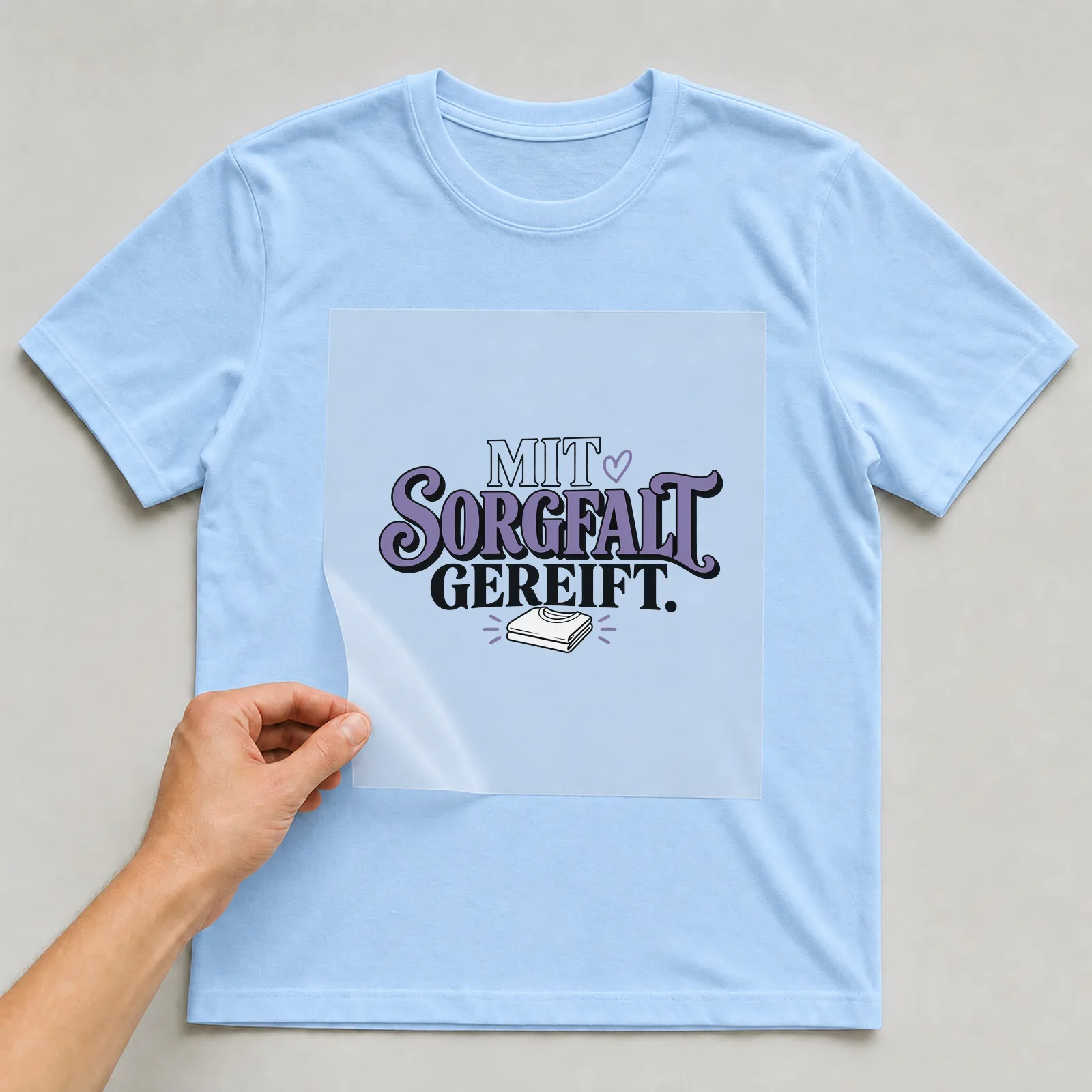 Bügelbild „Mit Sorgfalt gereift“ auf hellblauem T-Shirt, Folie wird aufgelegt