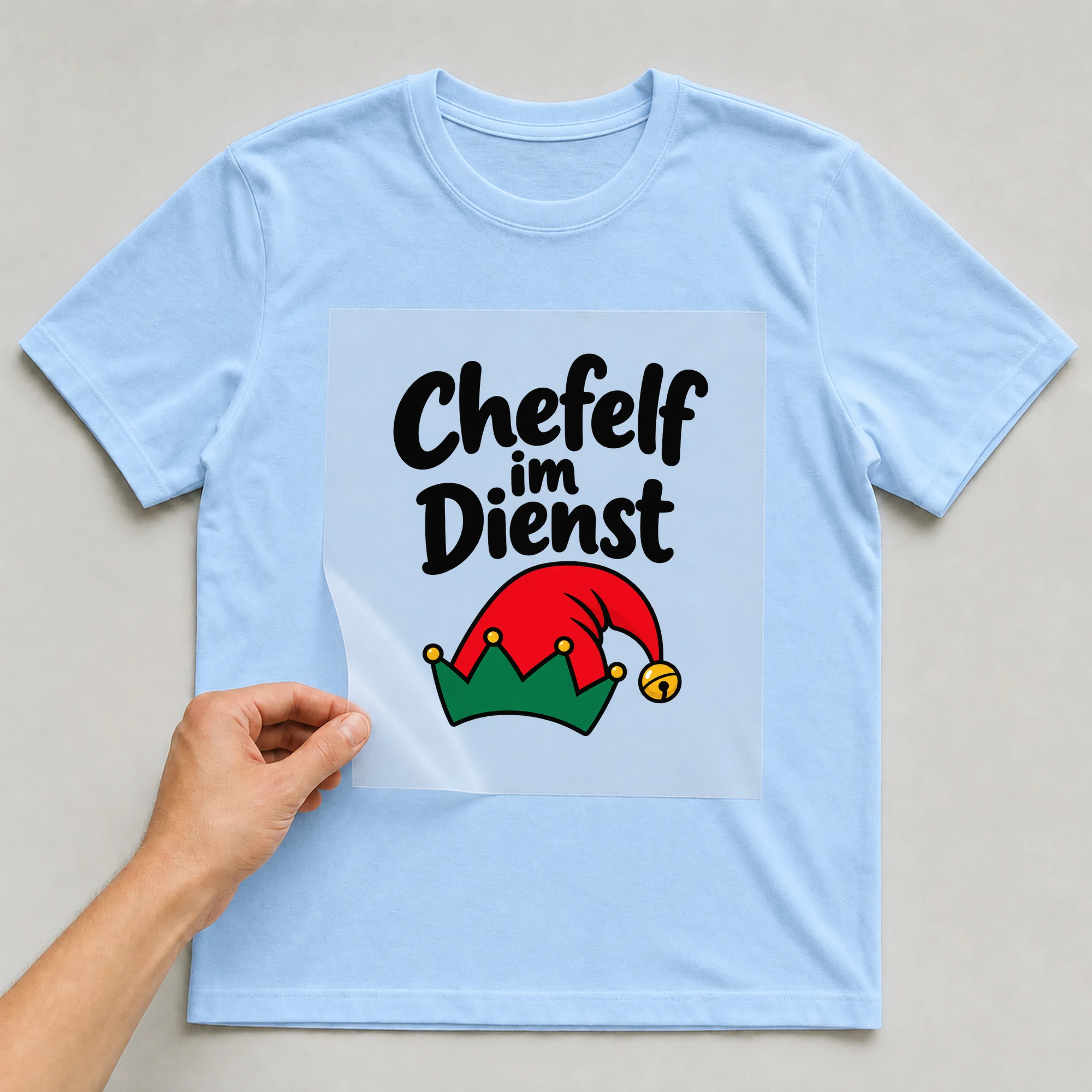 Bügelbild „Chefelf im Dienst“ auf babyblauem T-Shirt, Folie wird aufgelegt