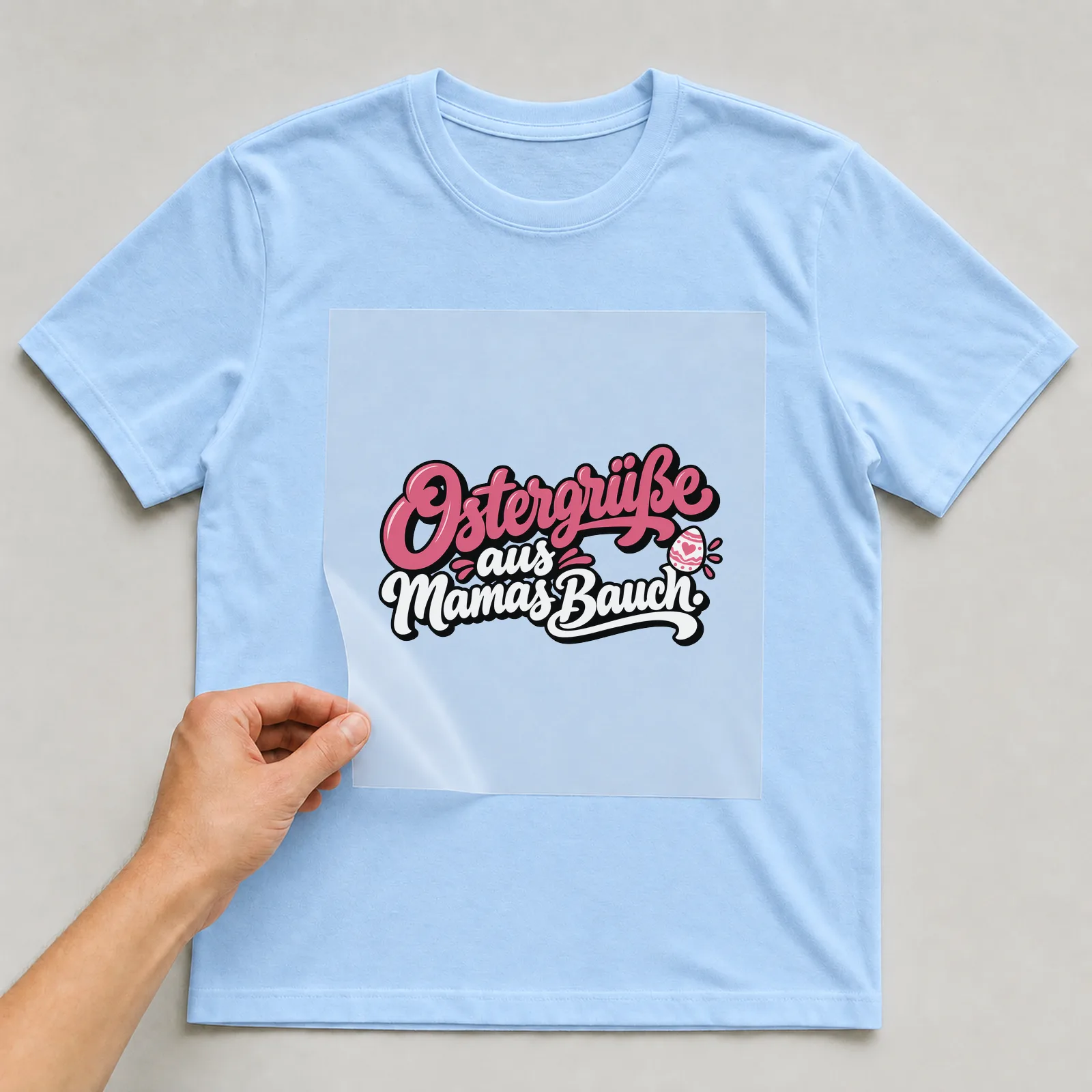 Bügelbild „Ostergrüße aus Mamas Bauch“ auf hellblauem T-Shirt, Folie wird aufgelegt