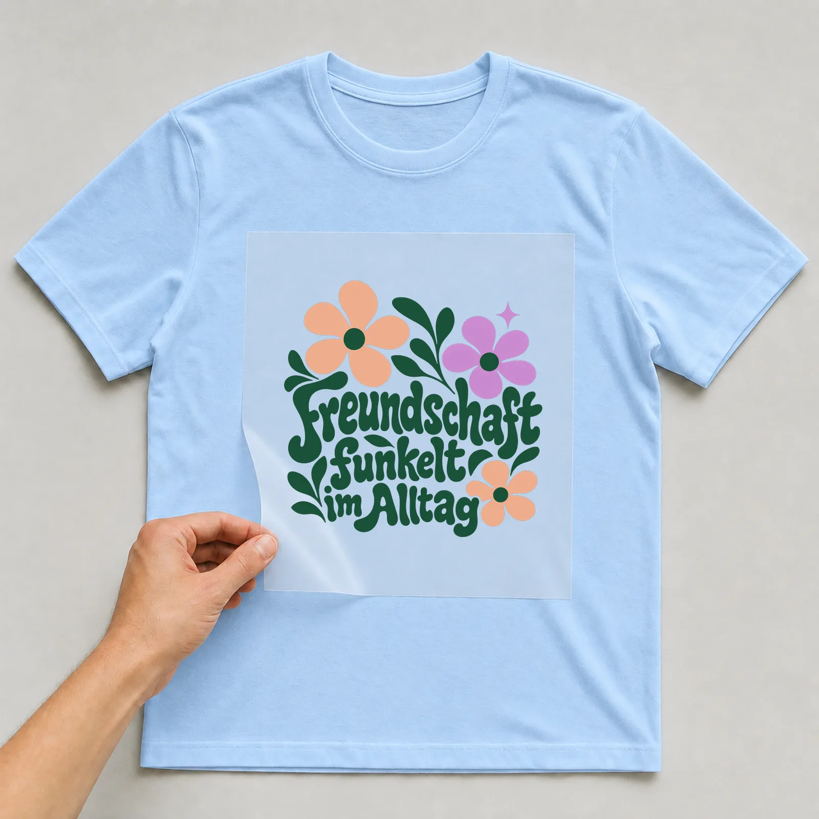 Bügelbild „Freundschaft funkelt im Alltag“ auf hellblauem T-Shirt, Folie wird aufgelegt