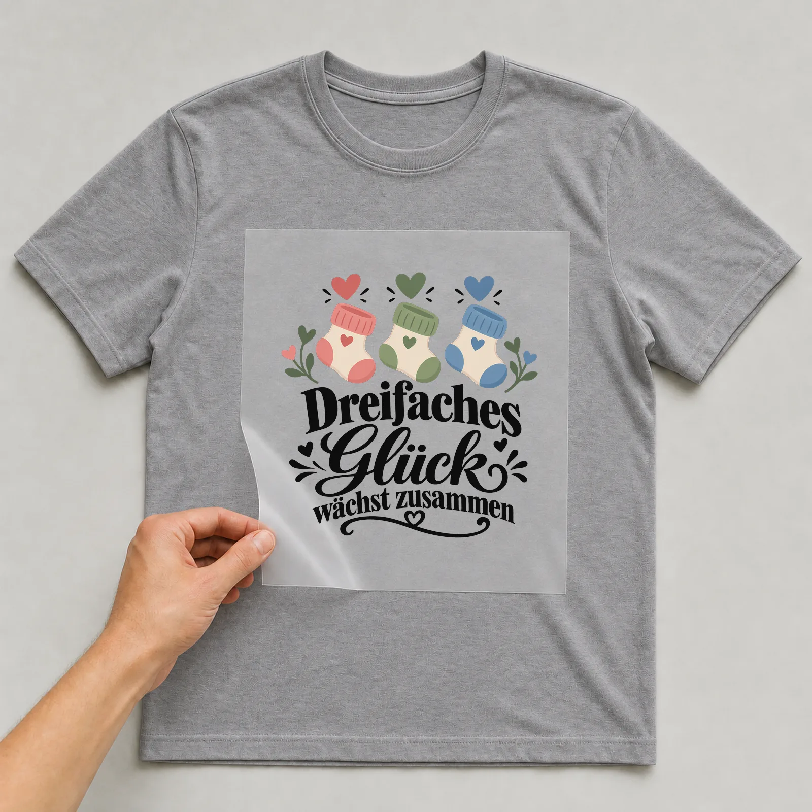 Bügelbild „Dreifaches Glück wächst zusammen“ auf grauem T-Shirt, Folie wird aufgelegt