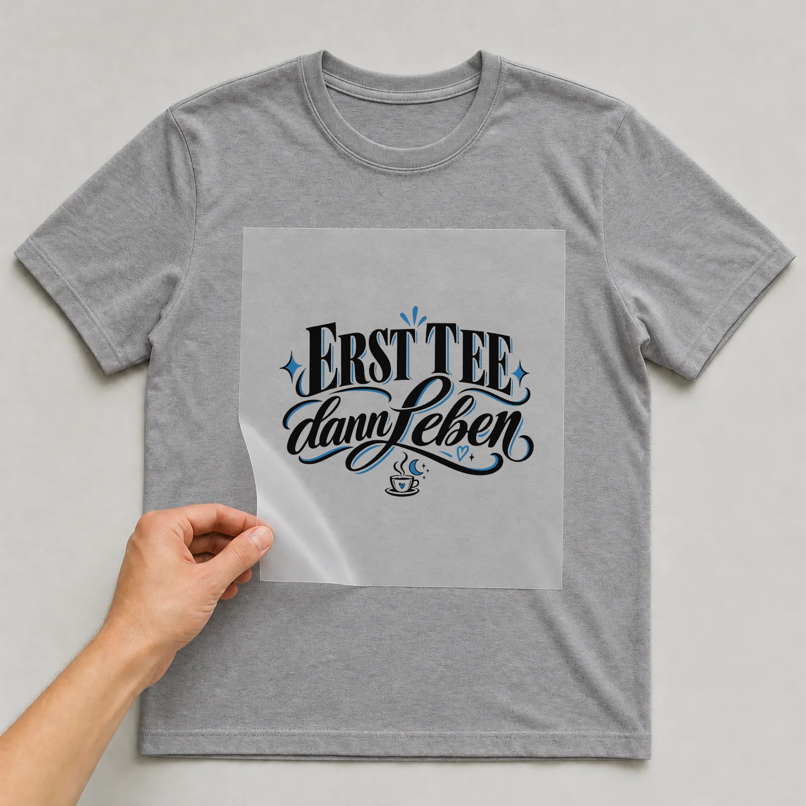 Bügelbild „Erst Tee dann Leben“ auf grauem T-Shirt, Folie wird aufgelegt
