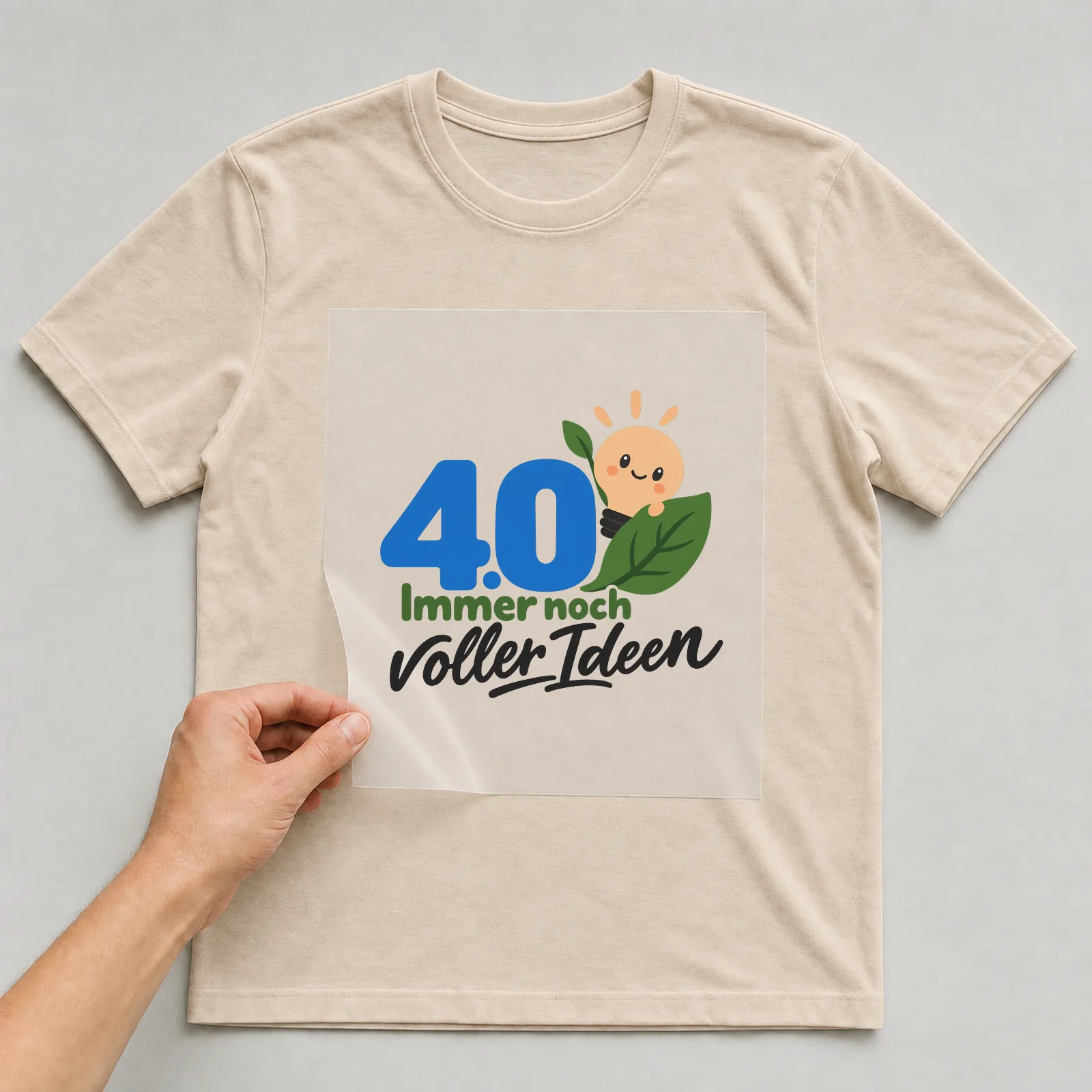 Bügelbild „40 · Immer noch voller Ideen“ auf beigem T-Shirt, Folie wird aufgelegt