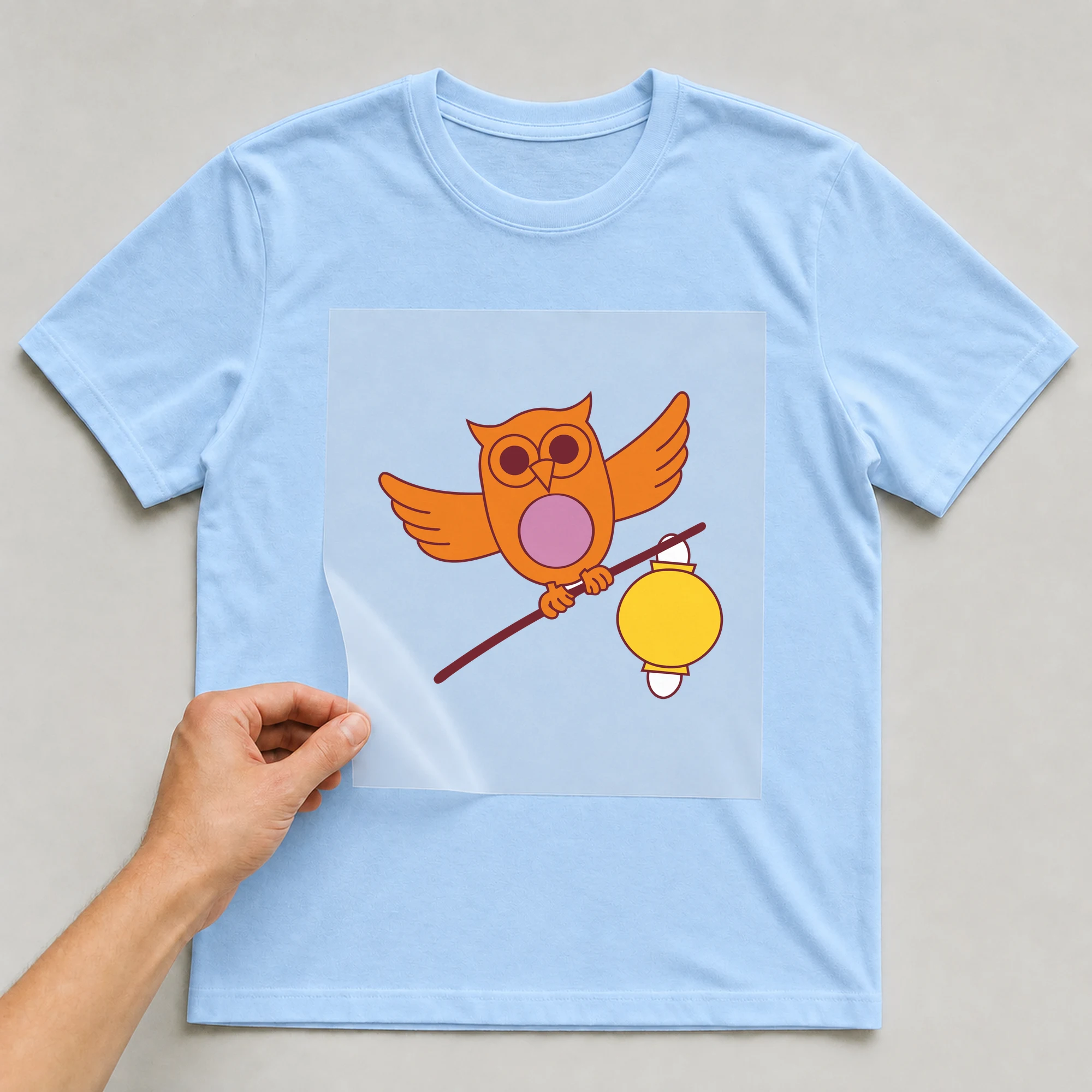 Bügelbild „Eule mit Laterne“ auf babyblauem T-Shirt, Folie wird aufgelegt