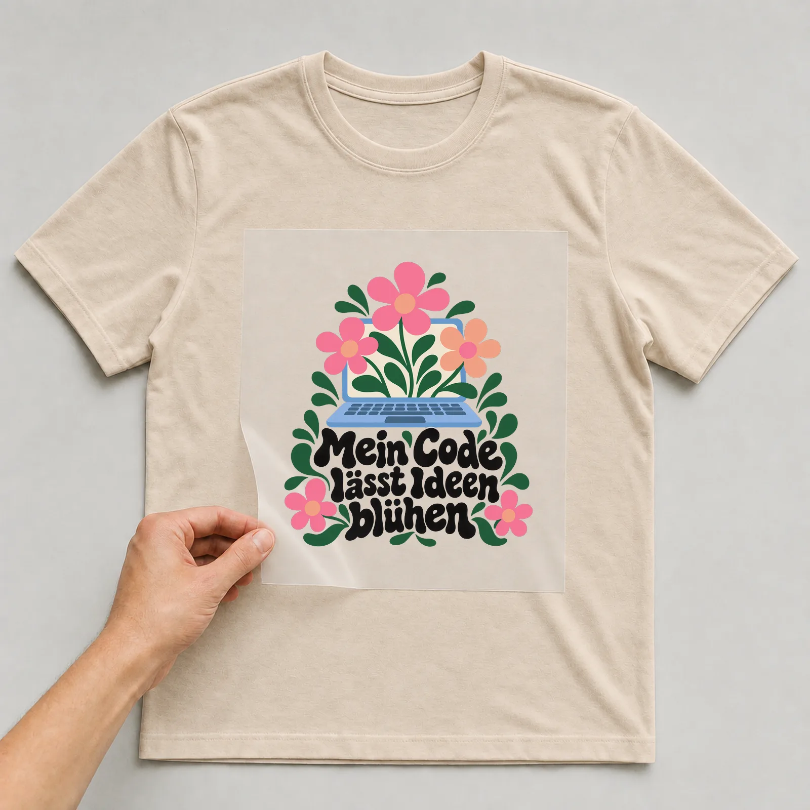 Bügelbild „Mein Code lässt Ideen blühen“ auf beigem T-Shirt, Folie wird aufgelegt
