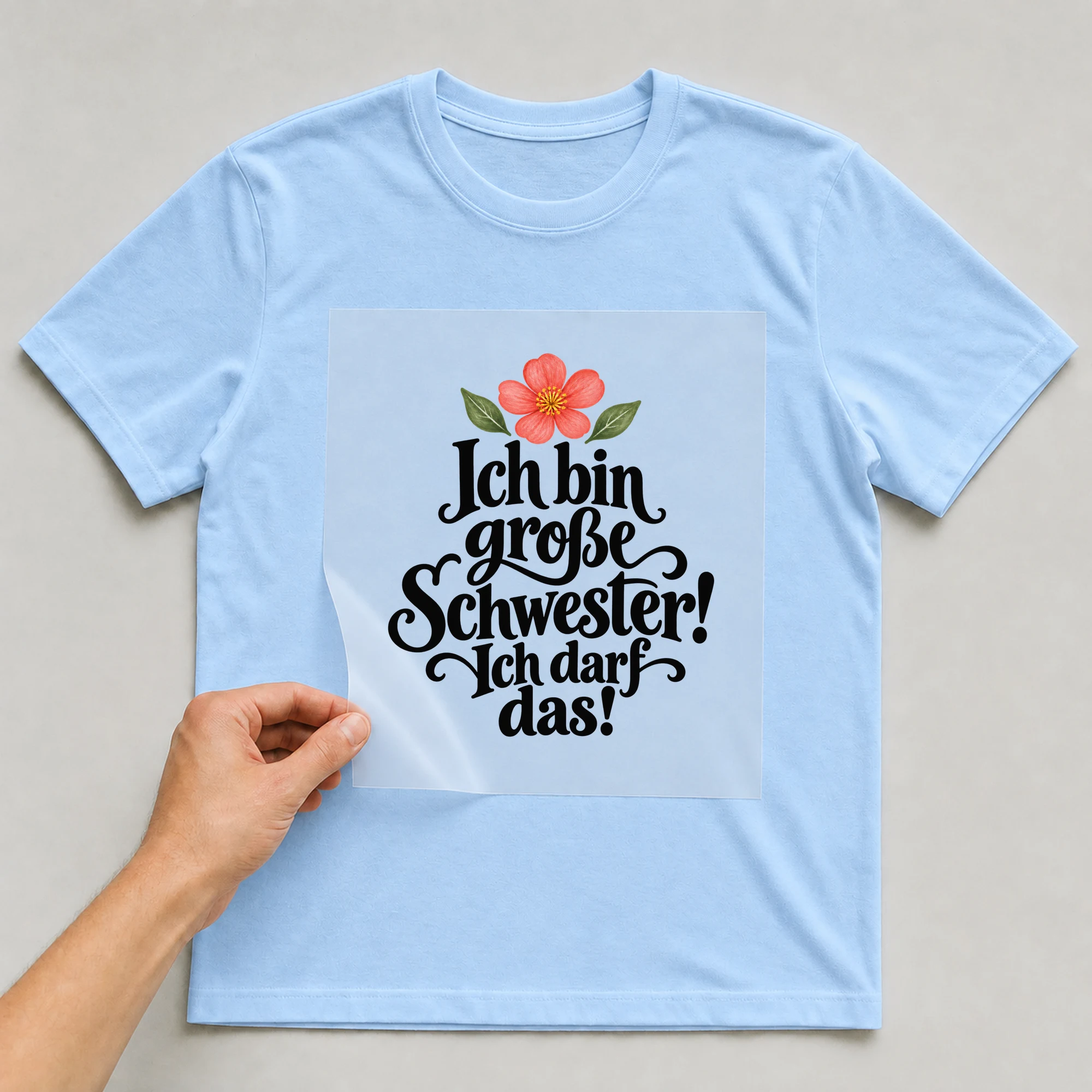 Bügelbild „Ich bin große Schwester! Ich darf das!“ auf babyblauem T-Shirt, Folie wird aufgelegt