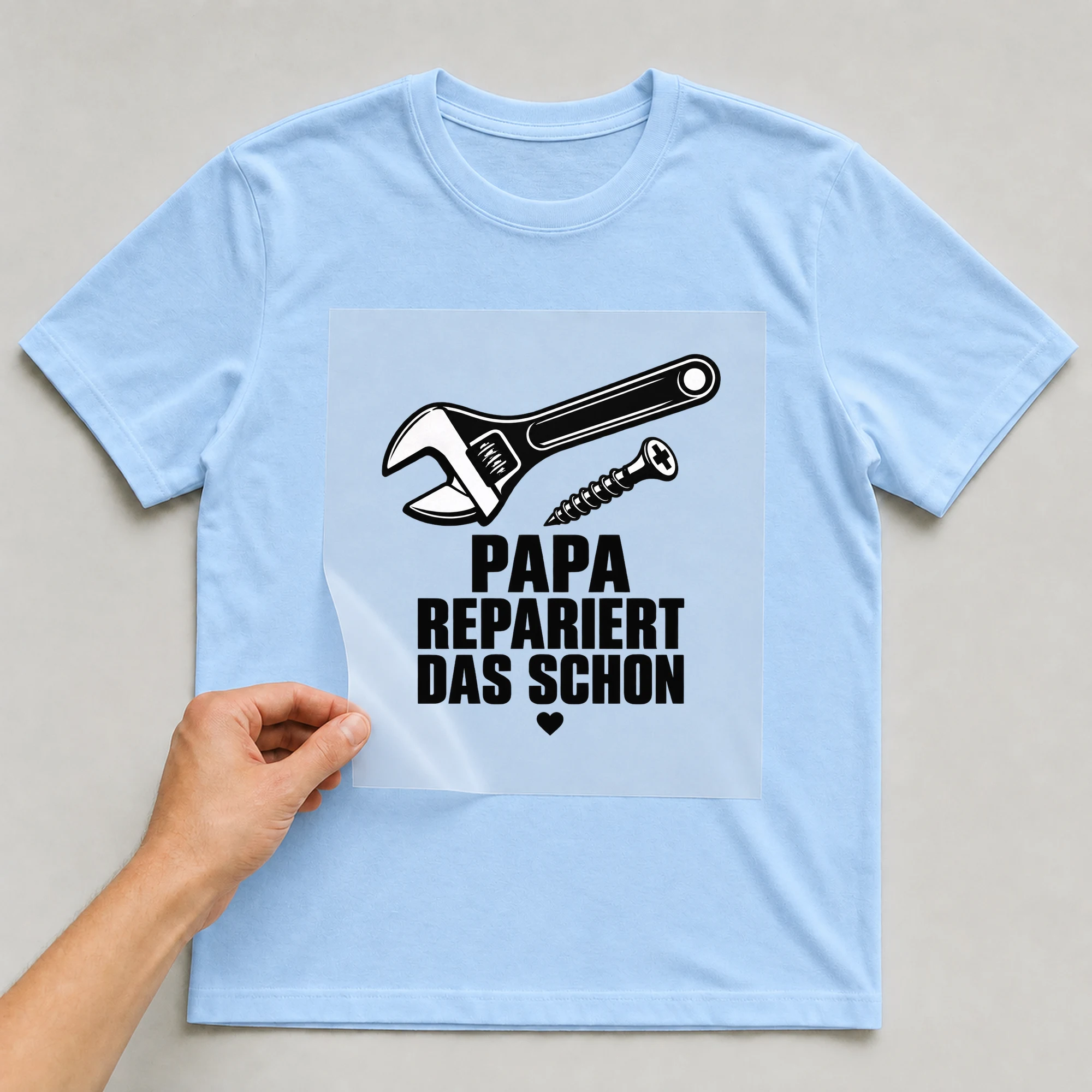 Bügelbild „Papa findet eine schraube weiter“ auf hellblauem T-Shirt, Folie wird aufgelegt