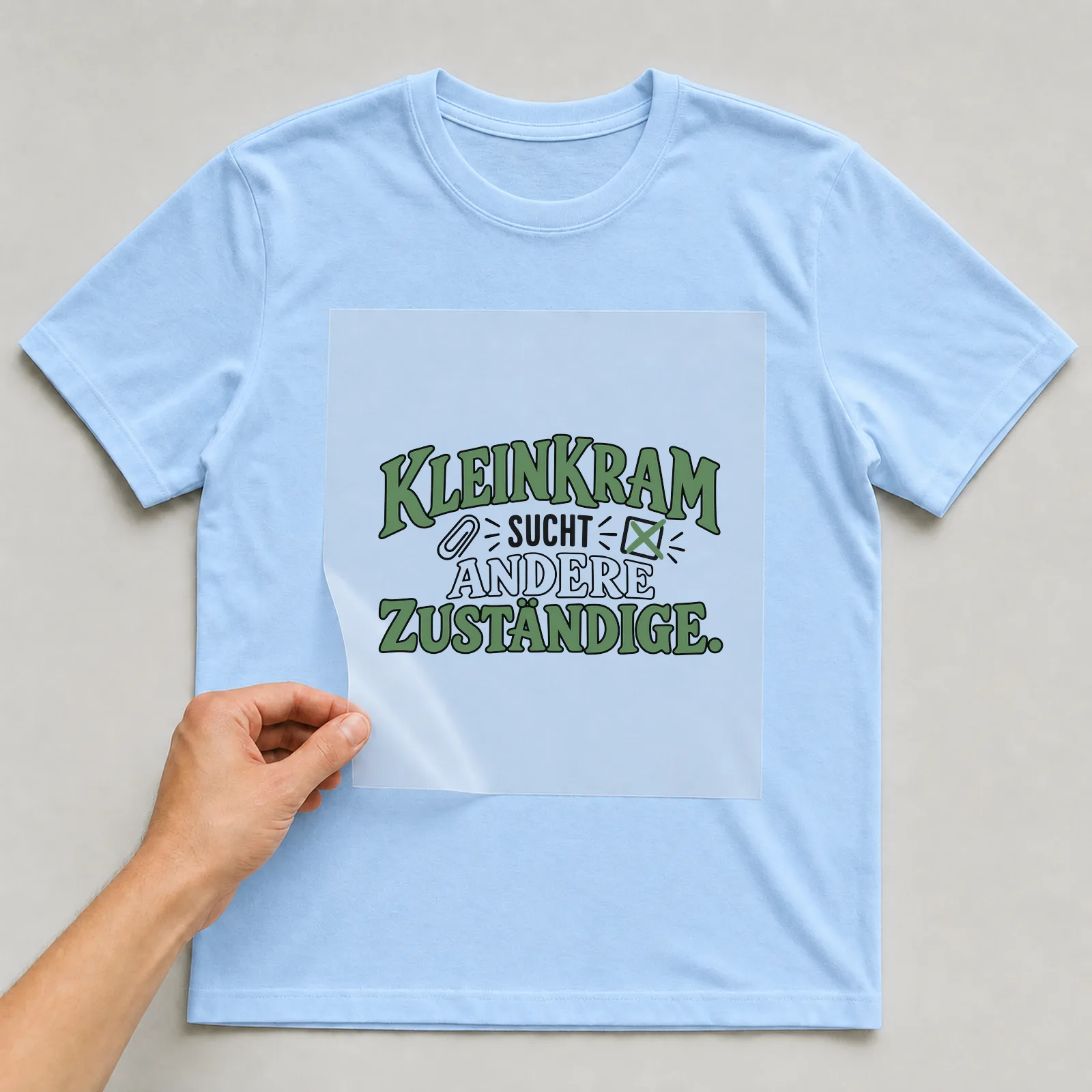Bügelbild „Kleinkram sucht andere zuständige“ auf hellblauem T-Shirt, Folie wird aufgelegt