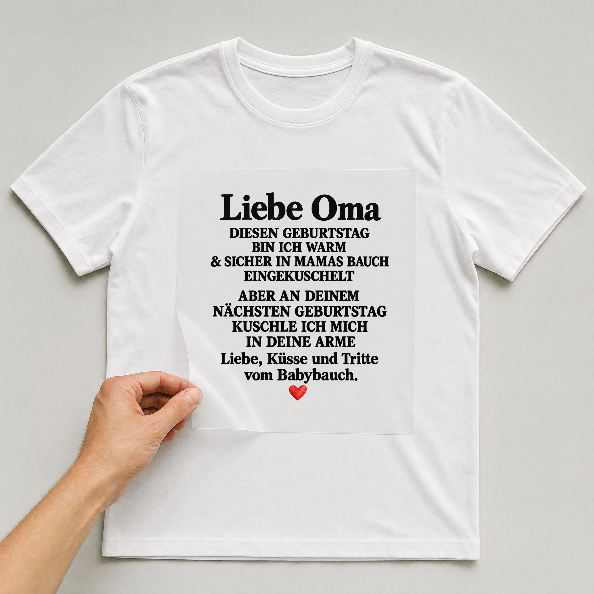 Bügelbild „Liebe Oma diesen Geburtstag bin ich warm & sicher in Mamas Bauch eingekuschelt“ auf weißem T-Shirt, Folie wird aufgelegt