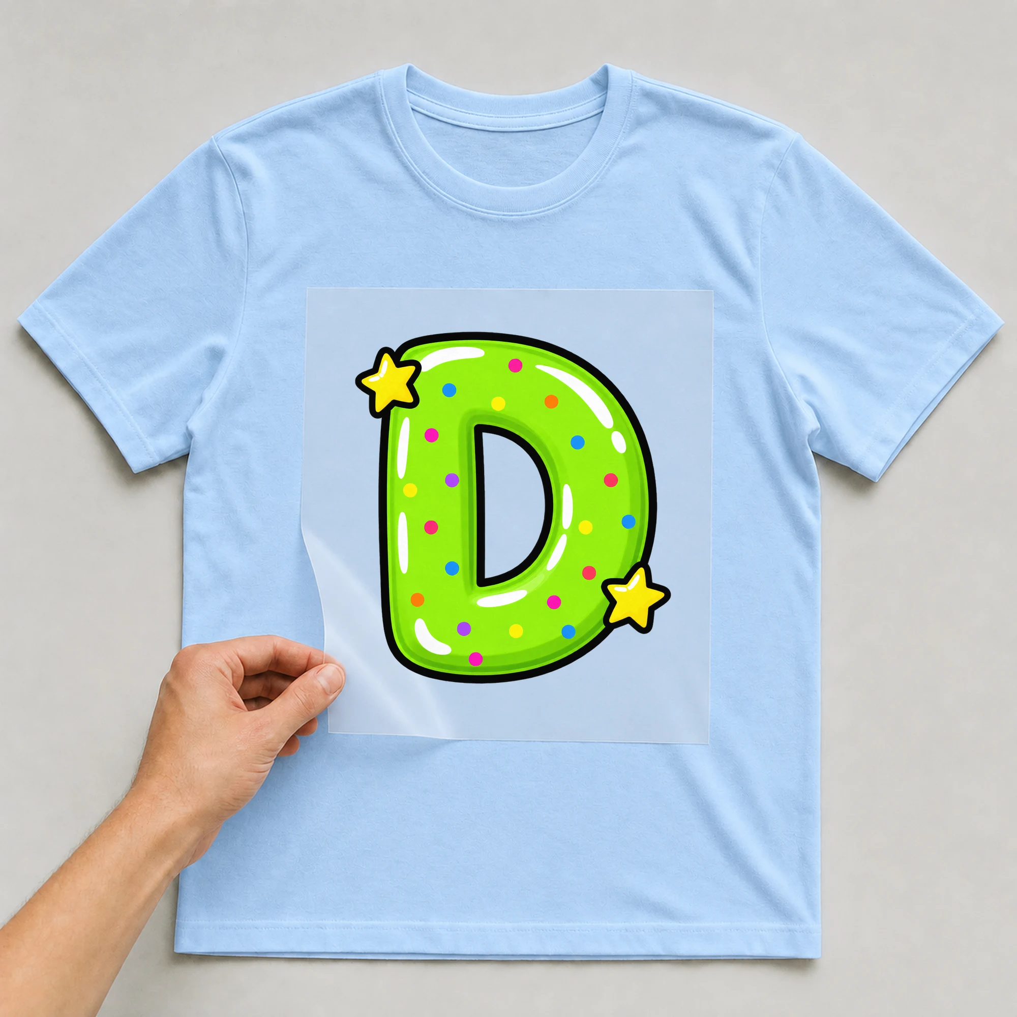 Bügelbild „Buchstabe D im Comic-Ballon-Stil“ auf babyblauem T-Shirt, Folie wird aufgelegt