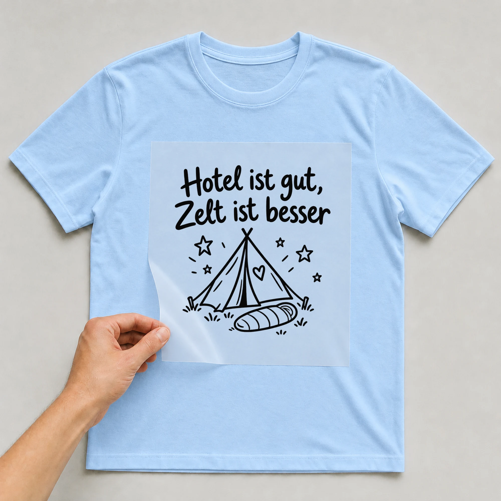 Bügelbild „Hotel ist gut, Zelt ist besser“ auf babyblauem T-Shirt, Folie wird aufgelegt
