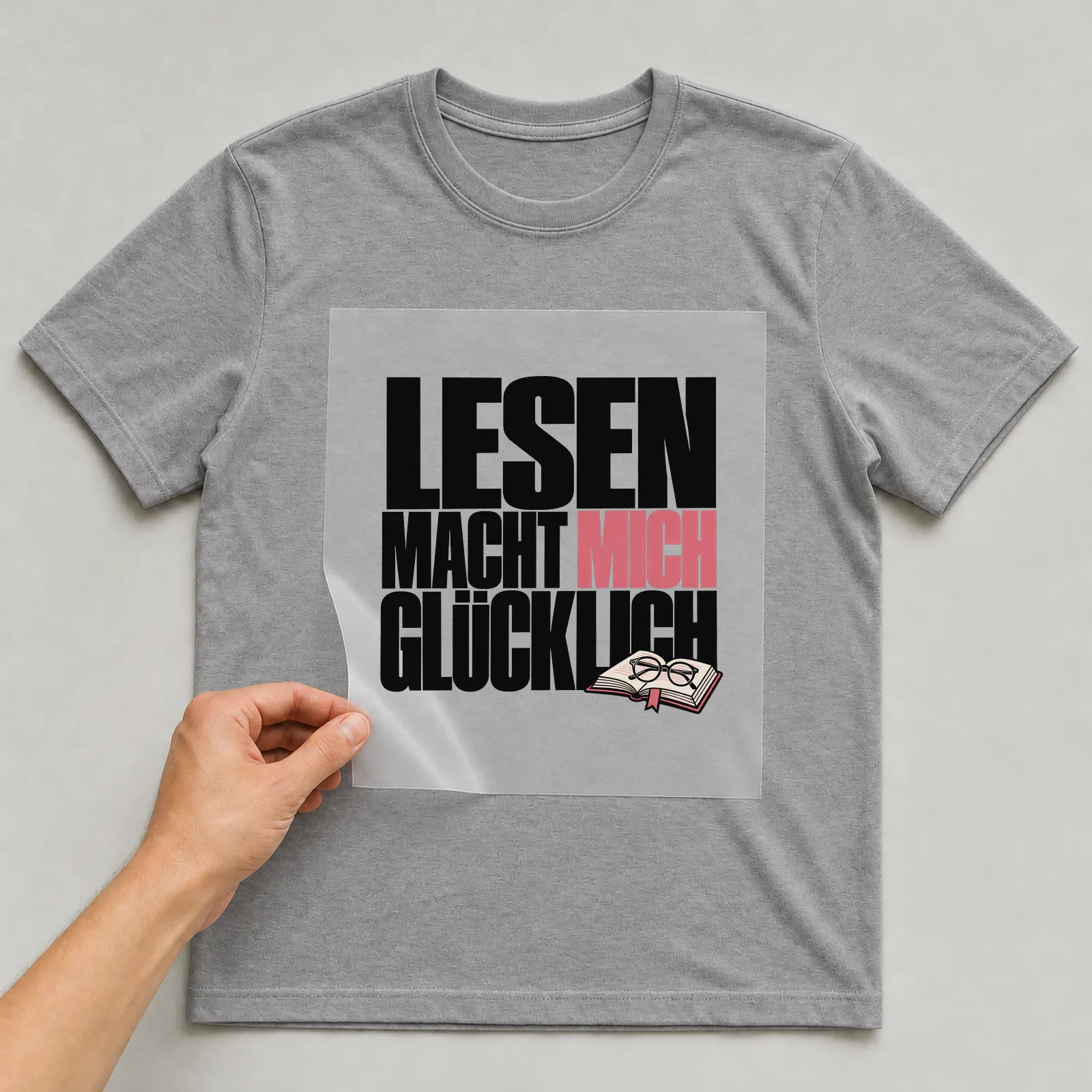 Bügelbild „Lesen macht mich glücklich“ auf grauem T-Shirt, Folie wird aufgelegt