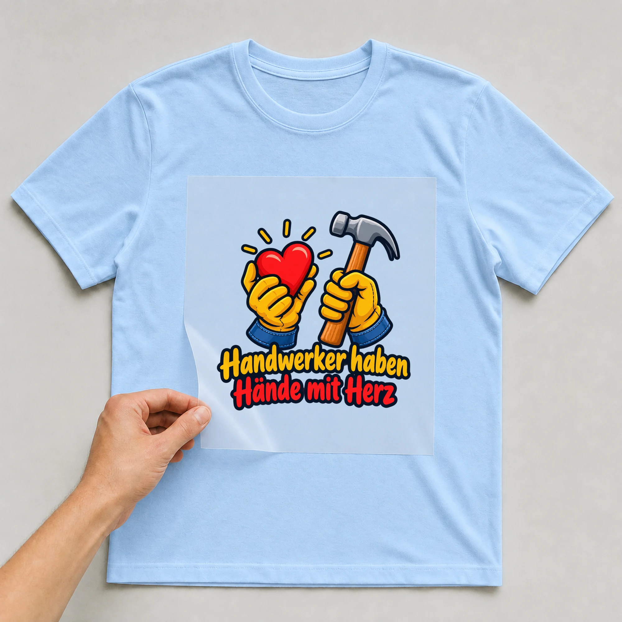 Bügelbild „Handwerker haben Hände mit Herz“ auf babyblauem T-Shirt, Folie wird aufgelegt