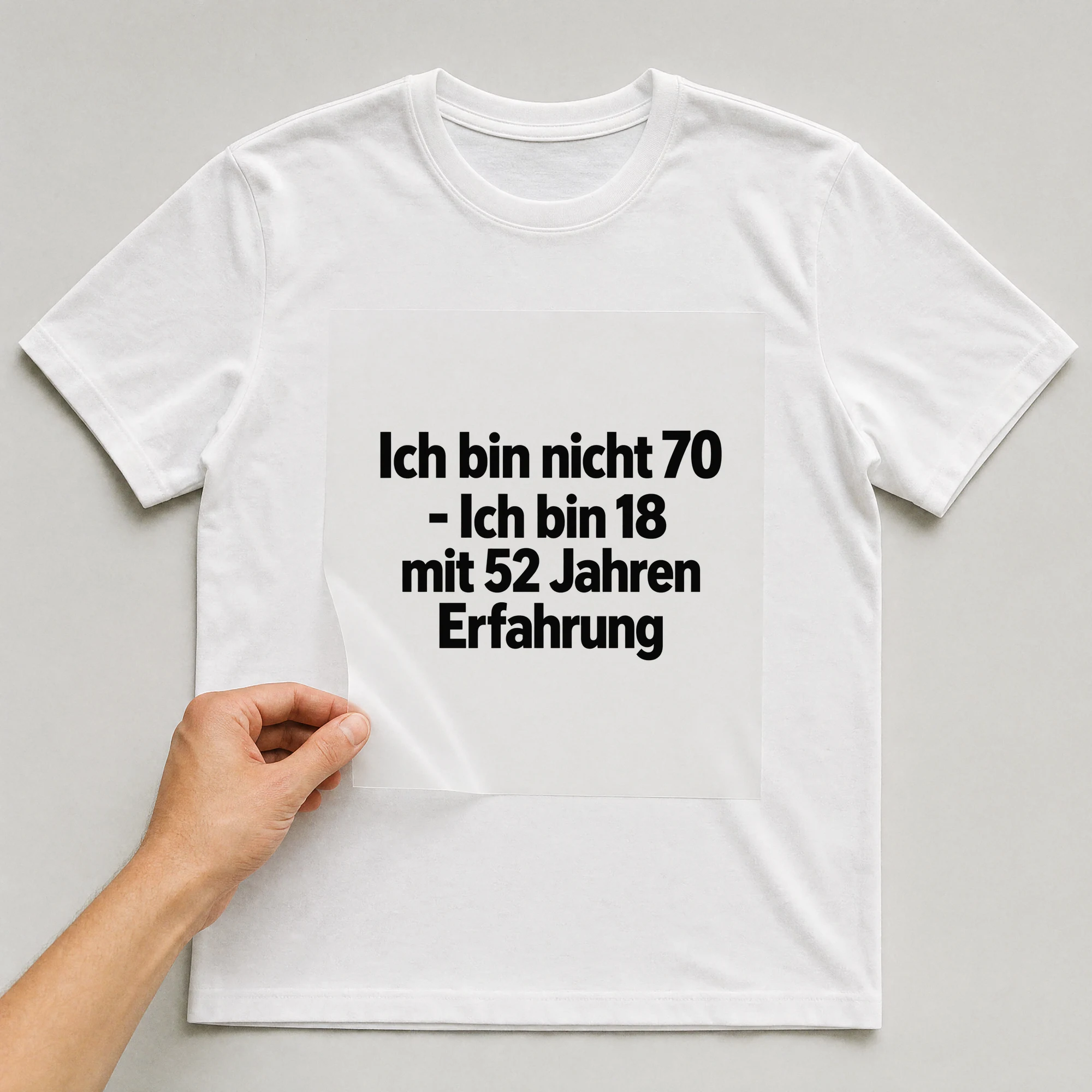Bügelbild „Ich bin nicht 70 - Ich bin 18 mit 52 Jahren Erfahrung“ auf weißem T-Shirt, Folie wird aufgelegt