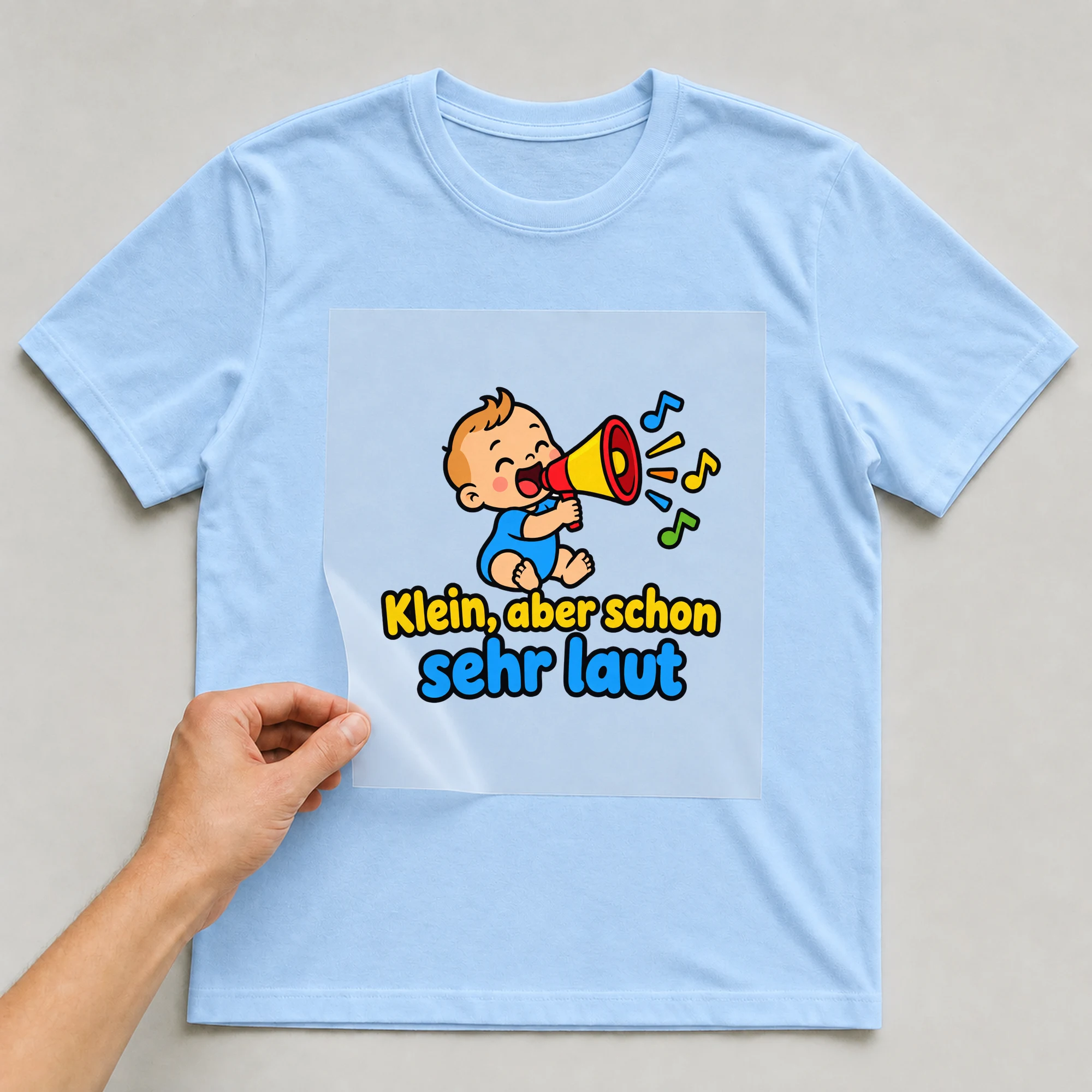 Bügelbild „Klein, aber schon sehr laut“ auf babyblauem T-Shirt, Folie wird aufgelegt