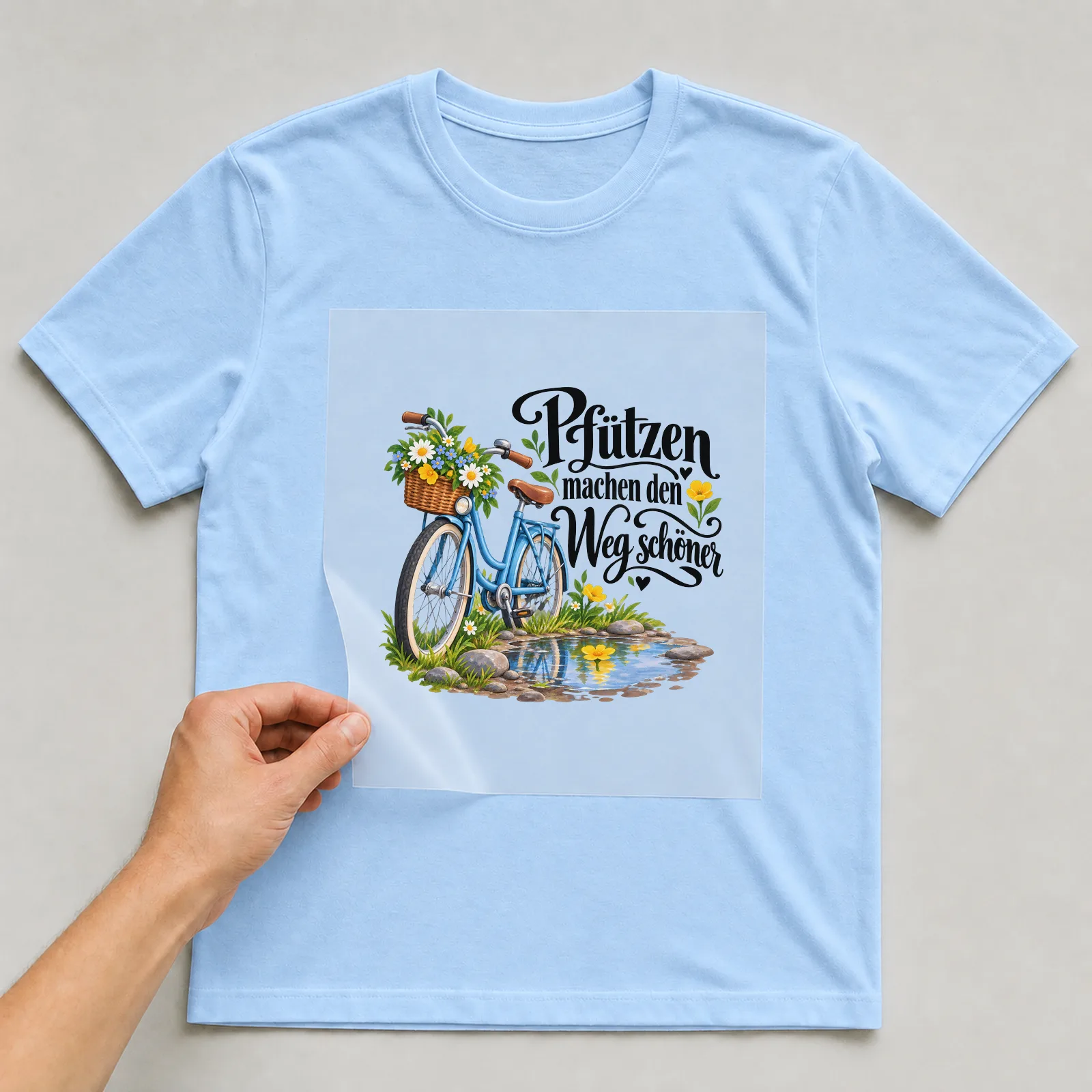 Bügelbild „Pfützen machen den Weg schöner“ auf hellblauem T-Shirt, Folie wird aufgelegt