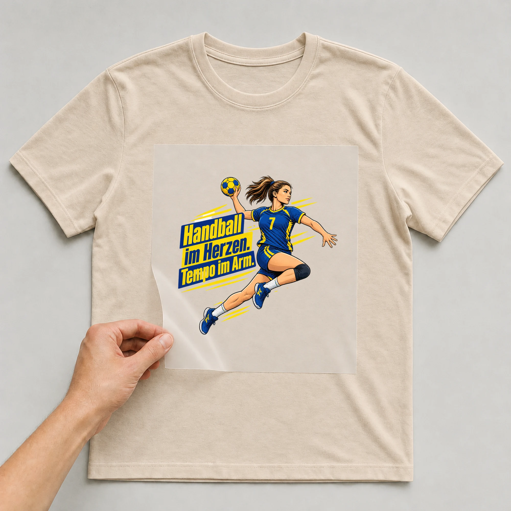 Bügelbild „Handball im Herzen. Tempo im Arm.“ auf beigem T-Shirt, Folie wird aufgelegt
