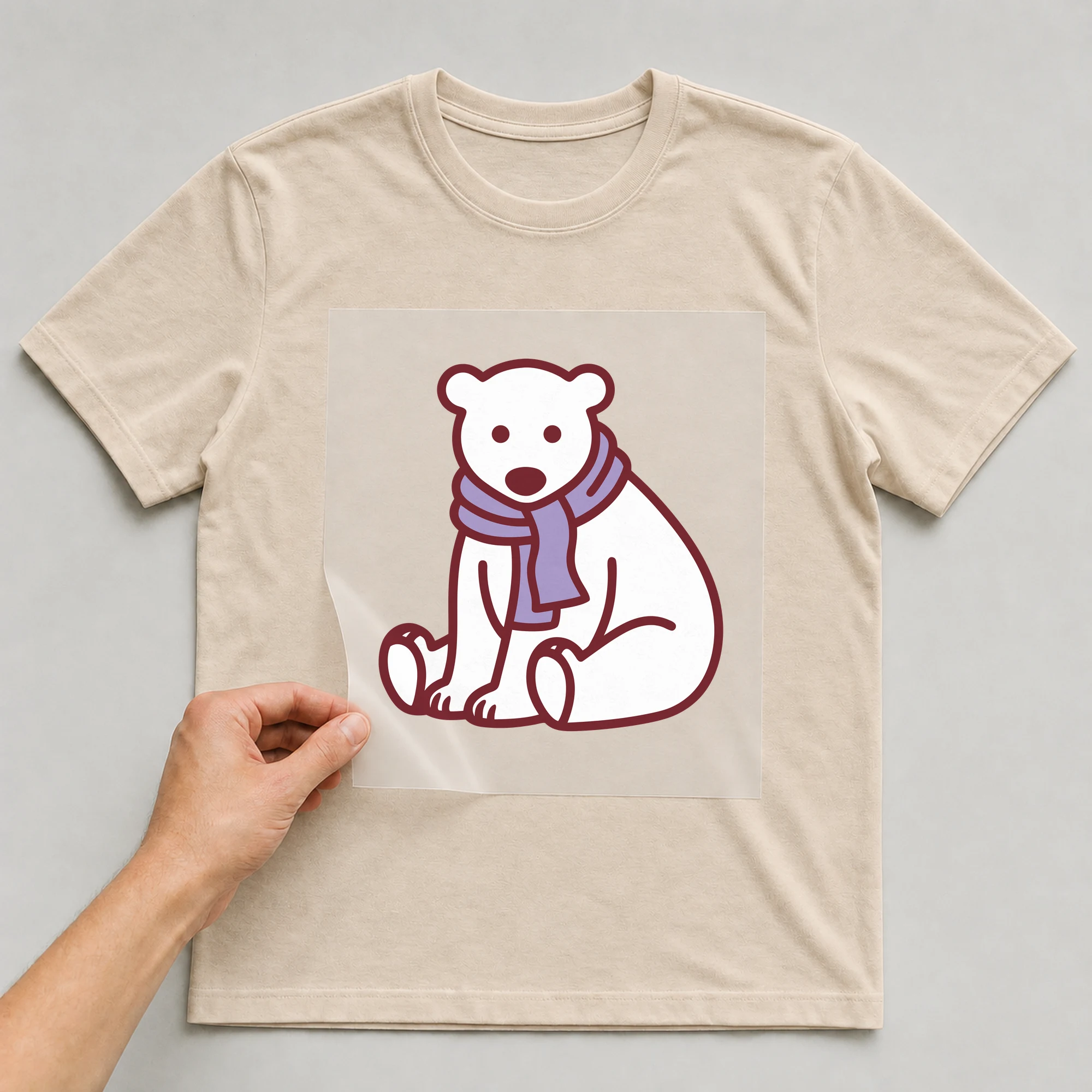 Bügelbild „Eisbär mit Schal“ auf beigem T-Shirt, Folie wird aufgelegt