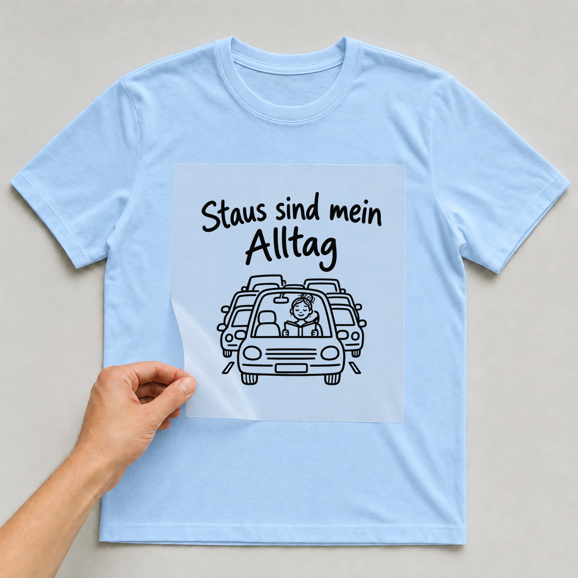 Bügelbild „Staus sind mein Alltag“ auf babyblauem T-Shirt, Folie wird aufgelegt