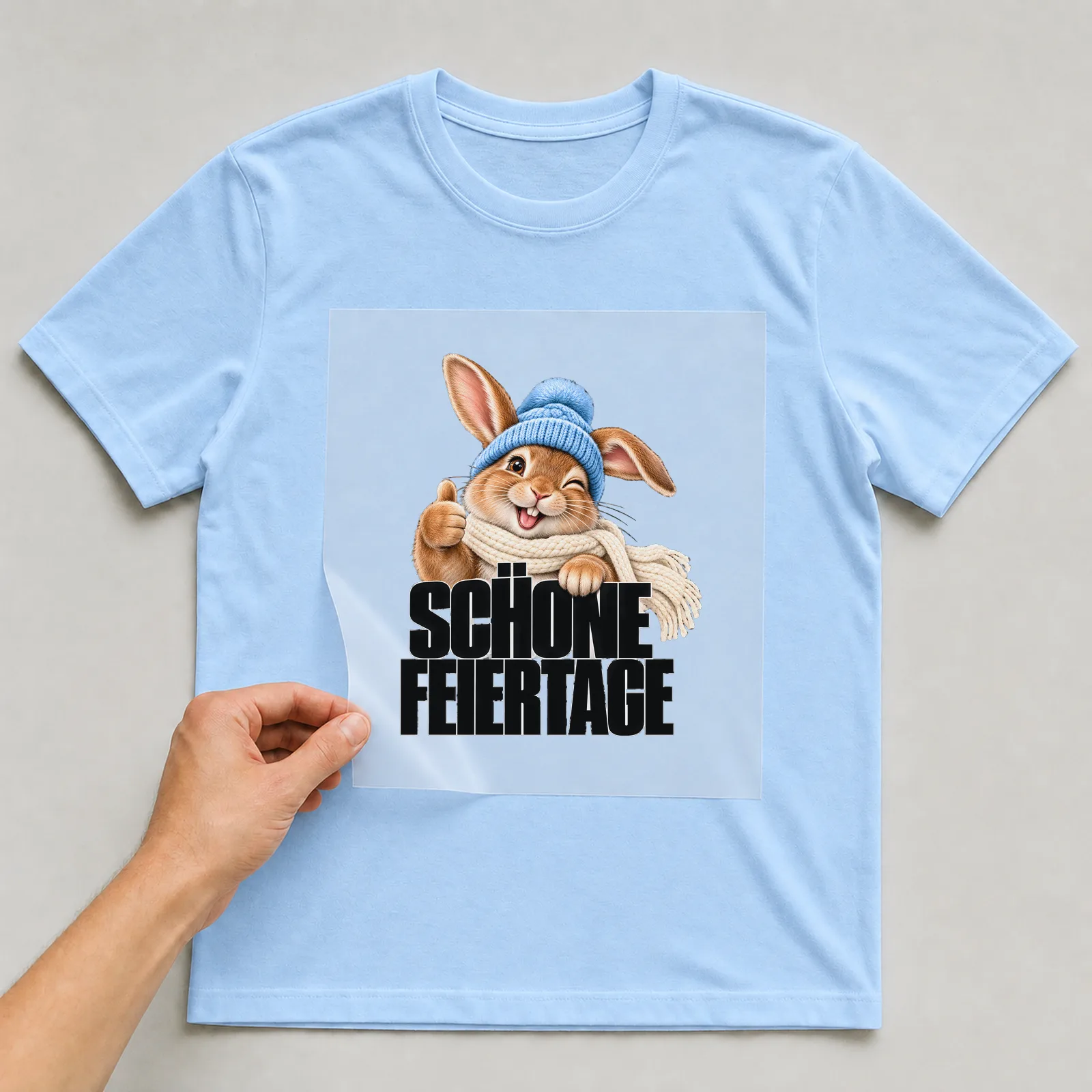 Bügelbild „Schöne Feiertage“ auf hellblauem T-Shirt, Folie wird aufgelegt