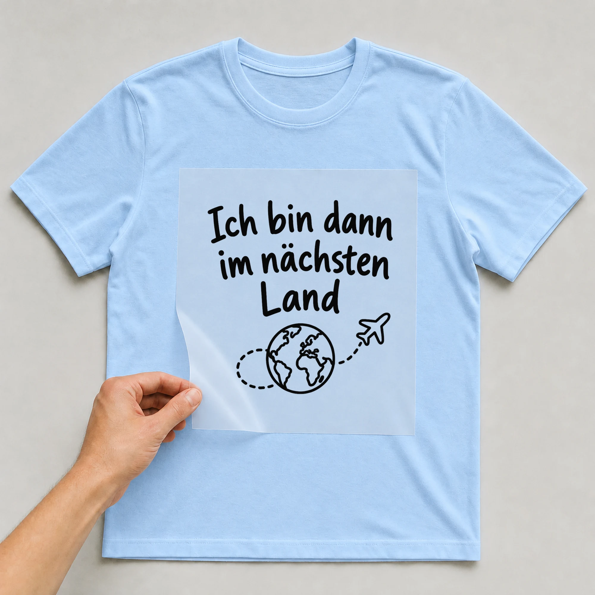 Bügelbild „Ich bin dann im nächsten Land“ auf babyblauem T-Shirt, Folie wird aufgelegt