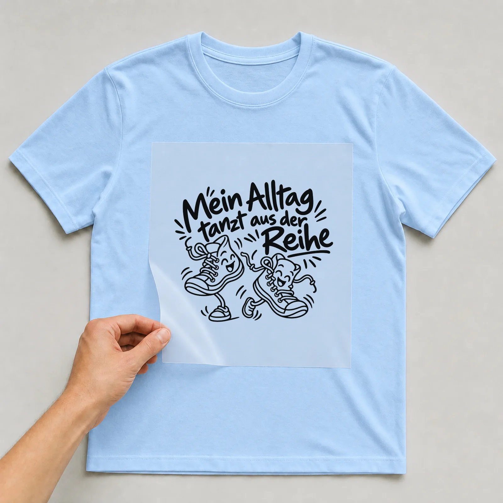 Bügelbild „Mein Alltag tanzt aus der Reihe“ auf hellblauem T-Shirt, Folie wird aufgelegt