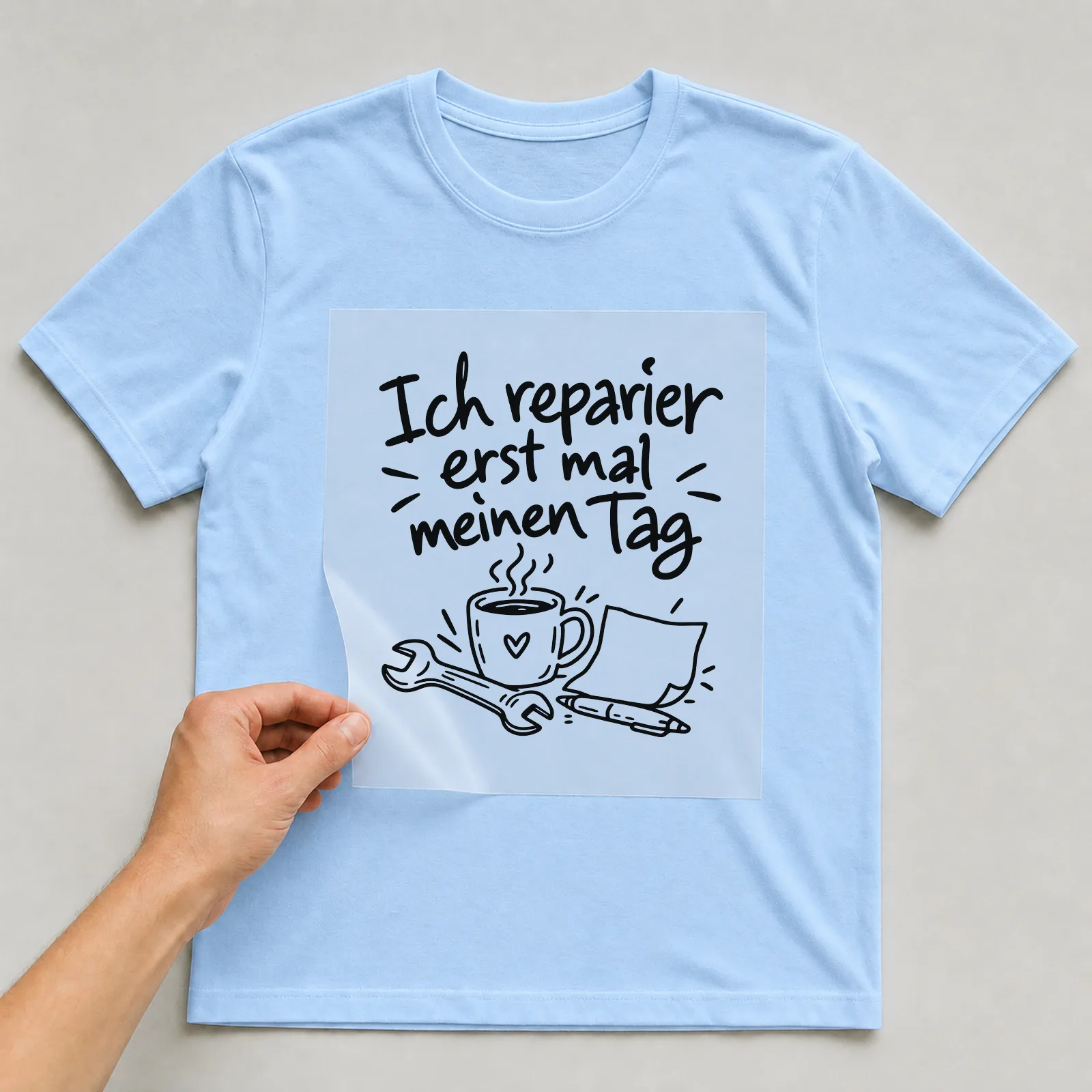 Bügelbild „Ich reparier erst mal meinen Tag“ auf hellblauem T-Shirt, Folie wird aufgelegt